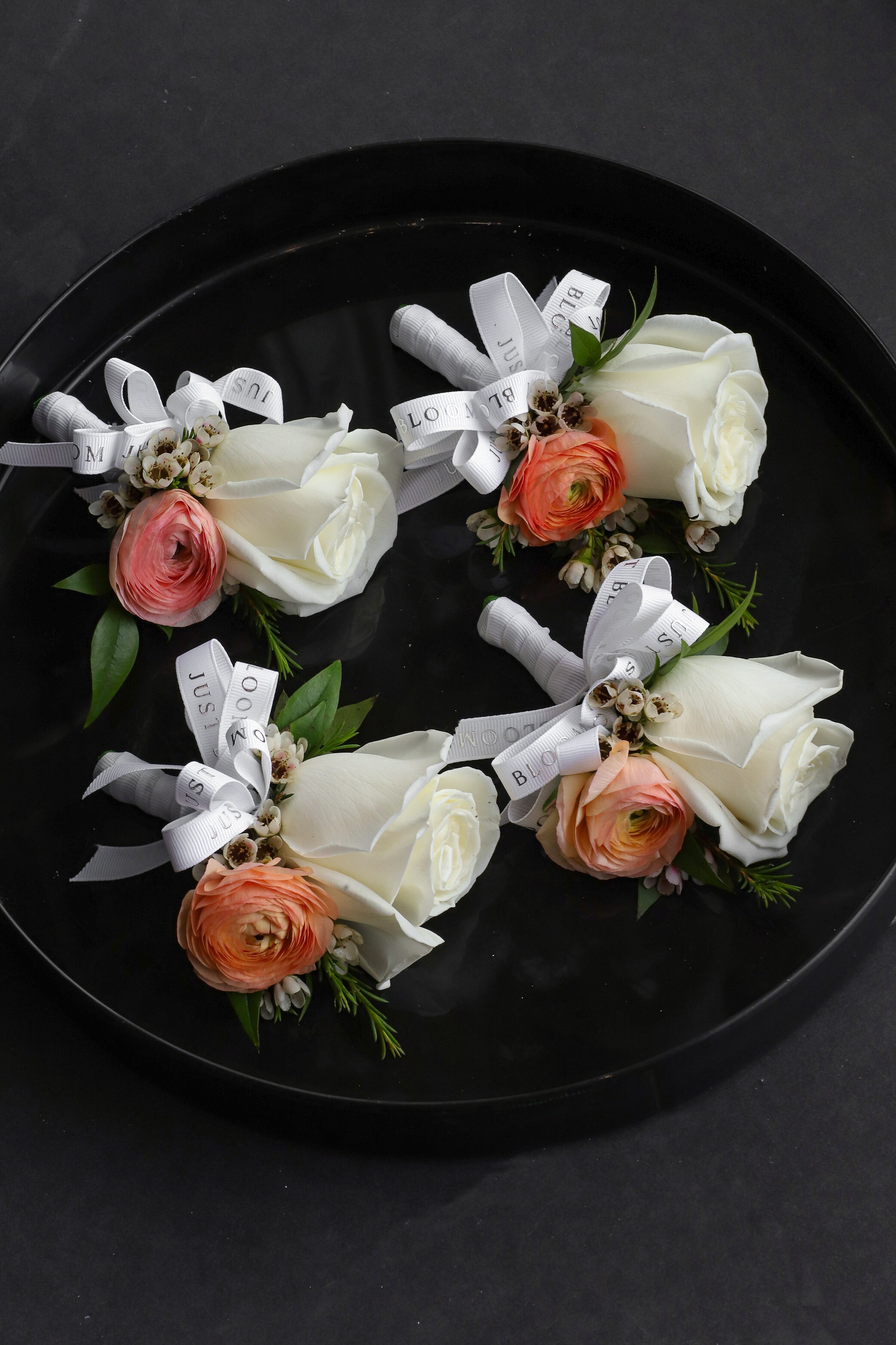 Four Dear One corsages arranged on a black tray featuring ivory Ecuadorian roses, peach ranunculus and wintersweet tied with Just Bloom white ribbon — Just Bloom Hong Kong