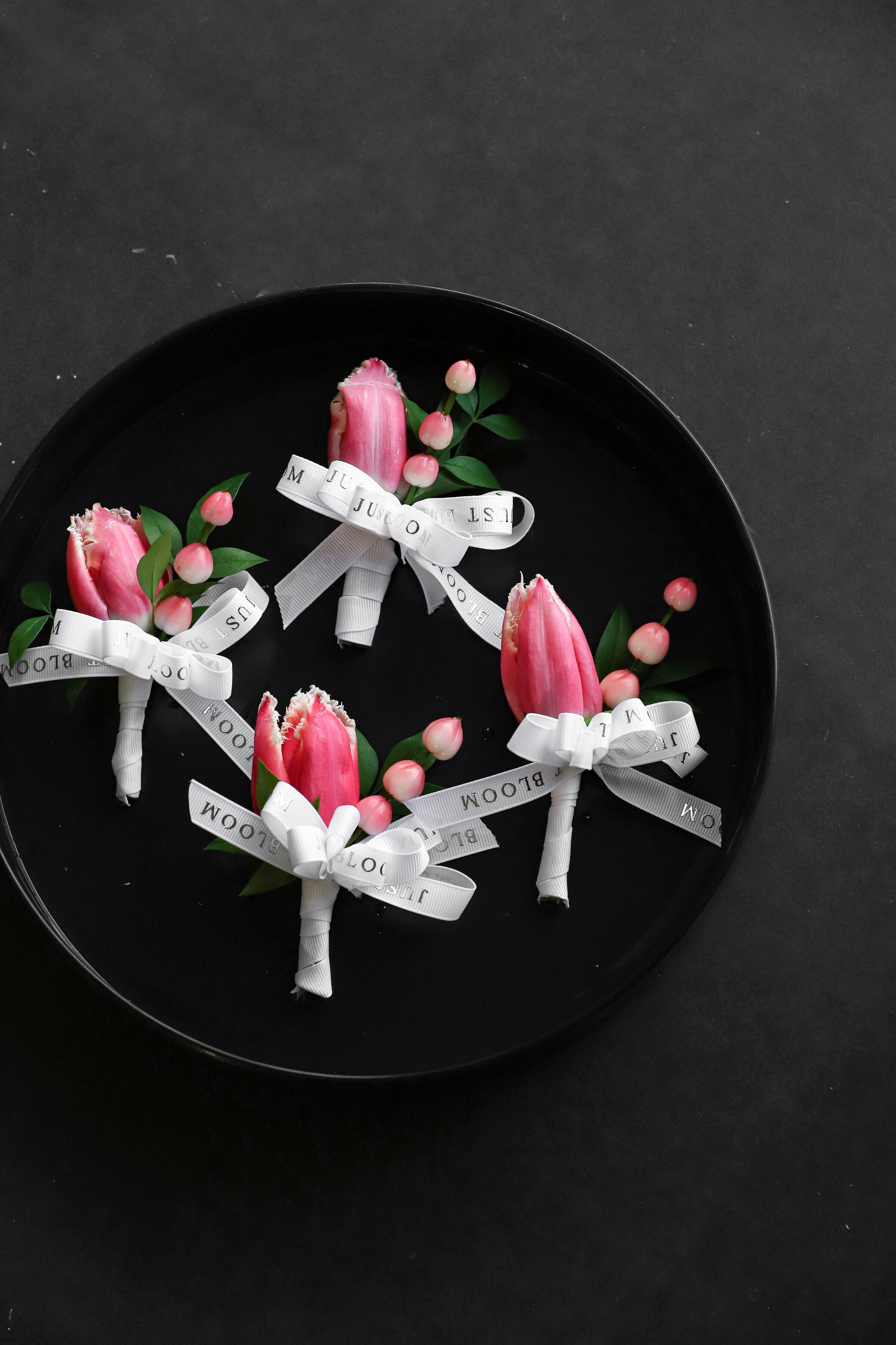 Close-up of four Boutonnieres on a black tray by Just Bloom Hong Kong, showcasing pink fringed tulips and hypericum berries with Just Bloom white ribbon