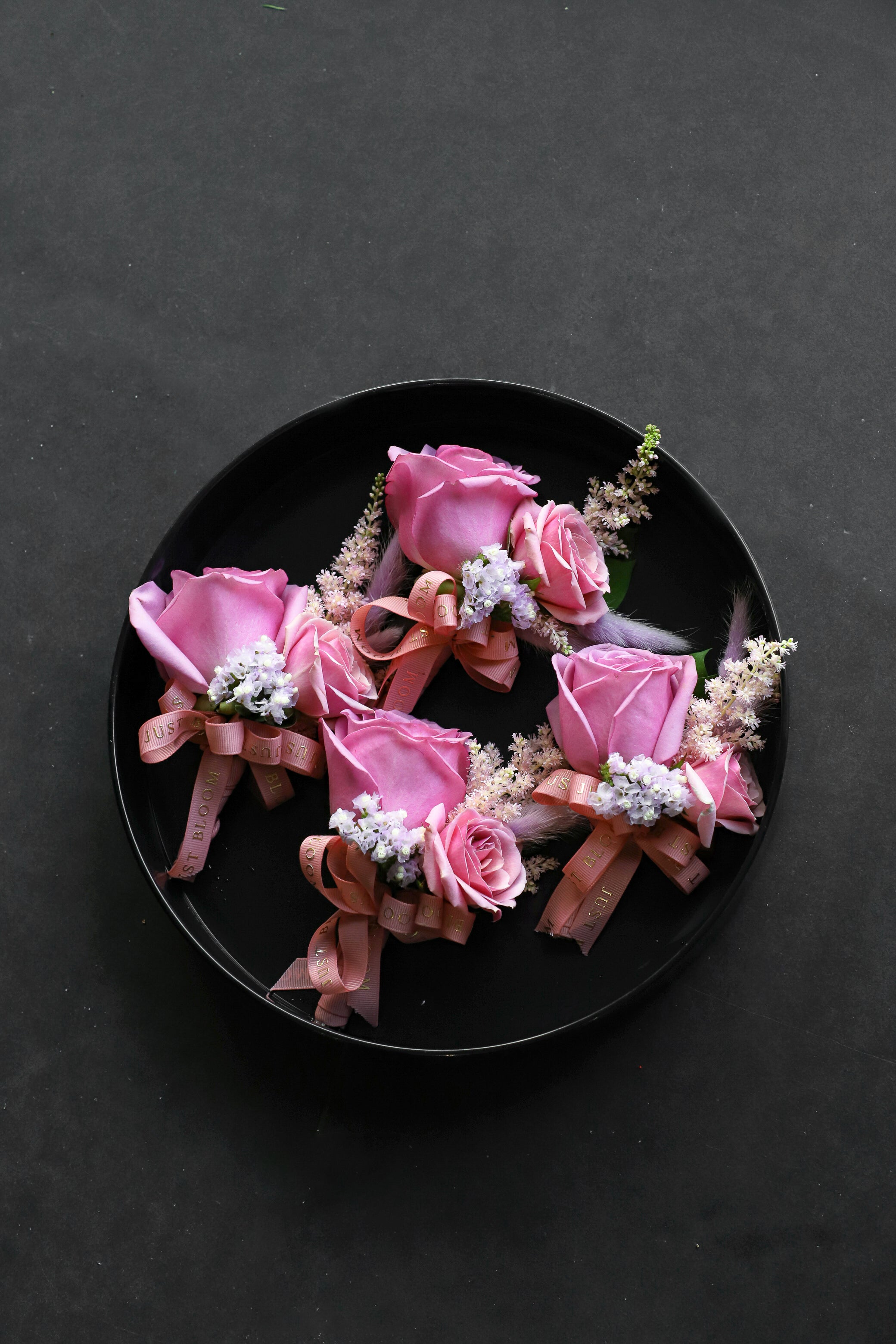 Four Boutonnieres arranged on a black tray featuring pink Ecuadorian roses, spray roses, pink astilbes and myosotis tied with Just Bloom rose gold ribbon — Just Bloom Hong Kong