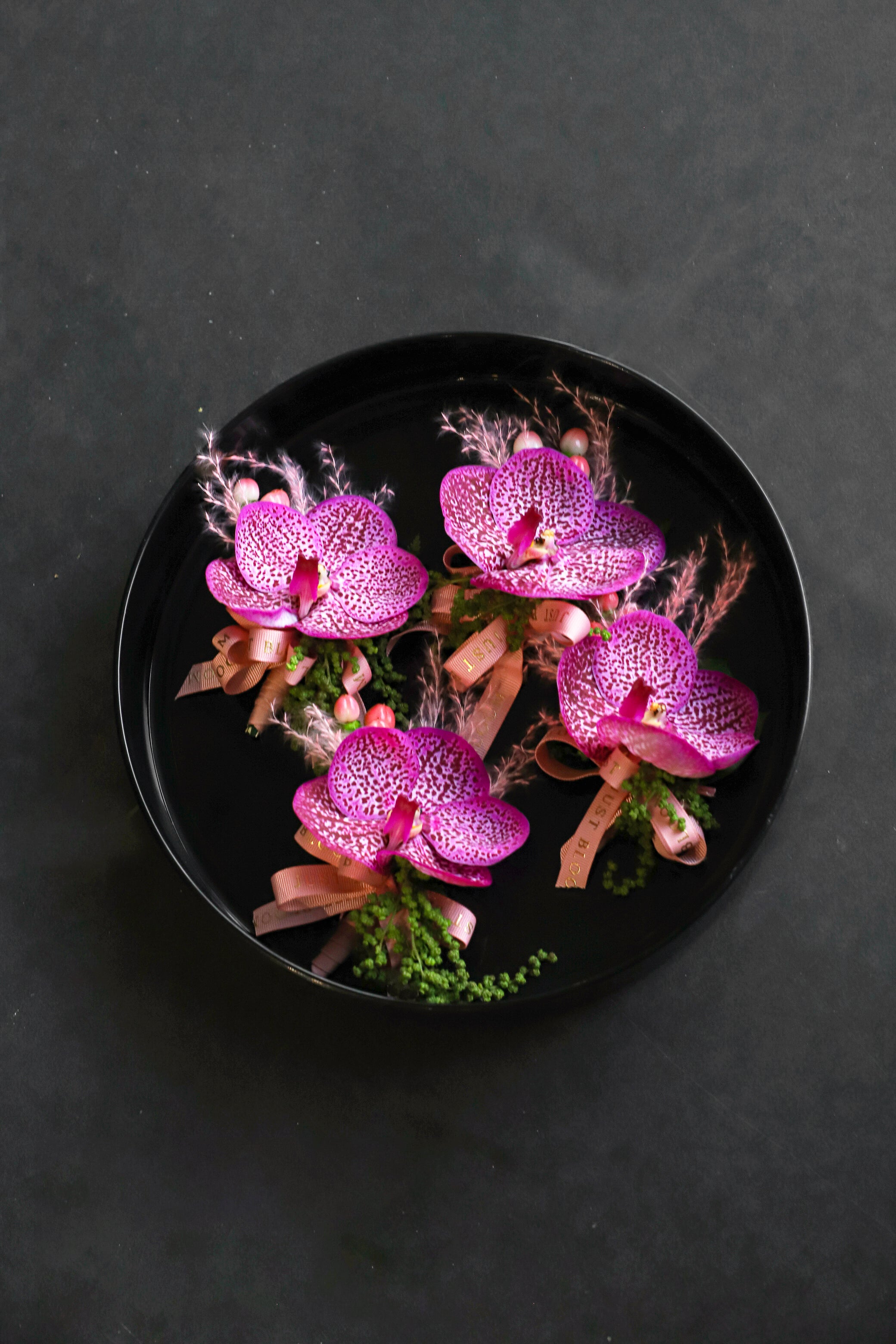  Four Boutonnieres Edit corsages arranged on a black tray featuring purple and pink vanda orchids, pink broom bloom and foliage tied with Just Bloom rose gold ribbon — Just Bloom Hong Kong