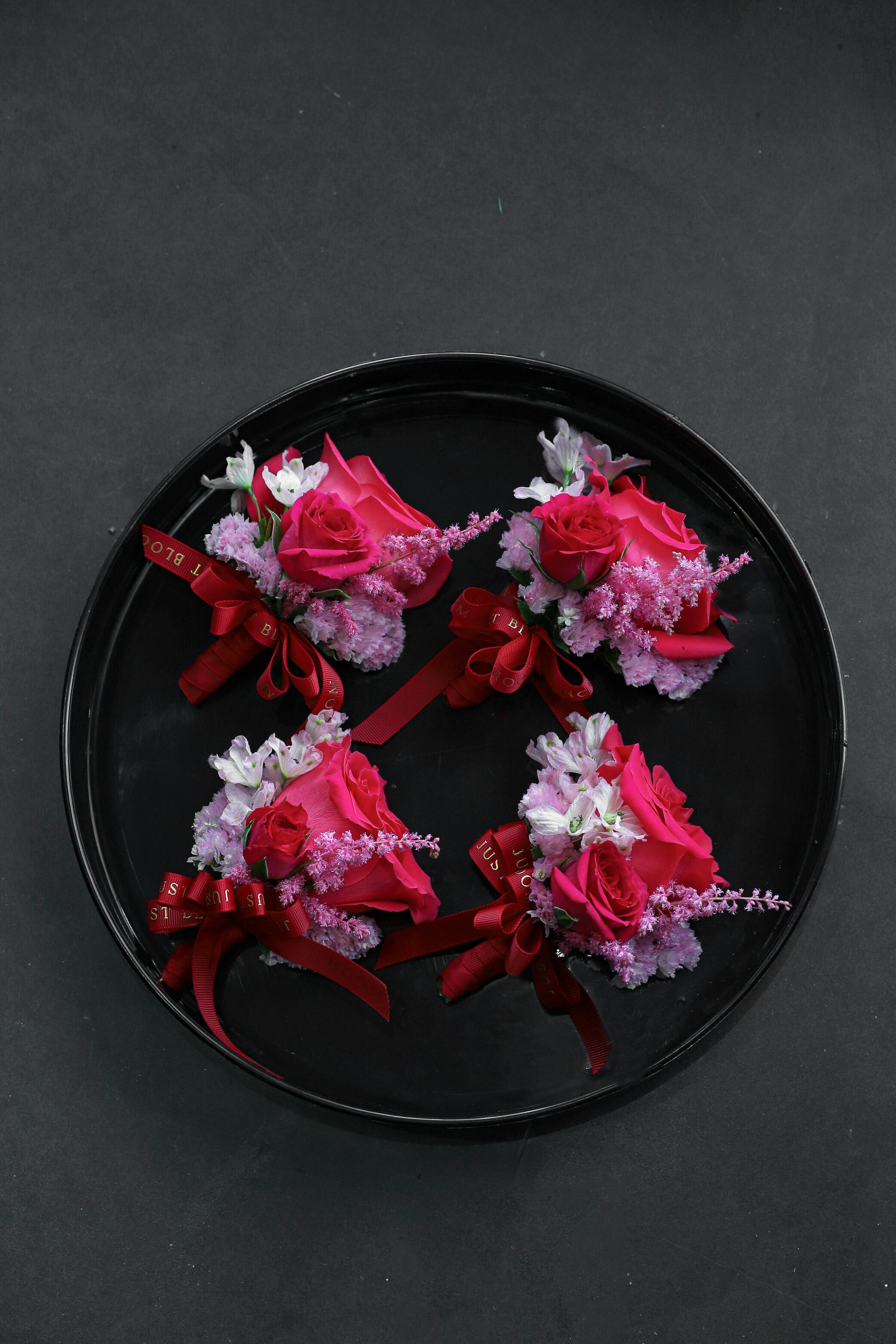  Four Boutonnieres arranged on a black tray featuring fuchsia Ecuadorian roses, deep pink astilbes, sweet peas and myosotis tied with Just Bloom deep red ribbon — Just Bloom Hong Kong