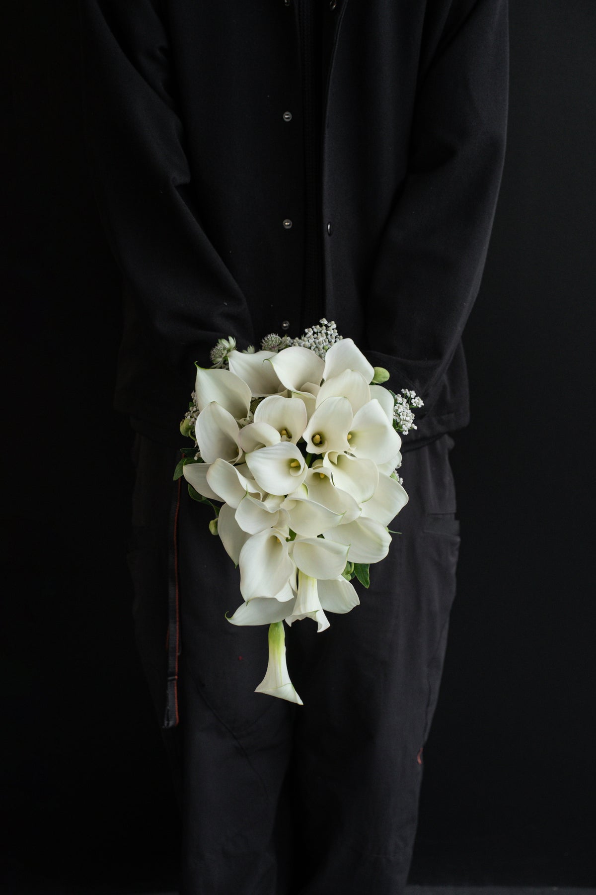 A Lifetime with You bridal bouquet held at the side by a model in a black outfit, showing the full cascade length against a dark background