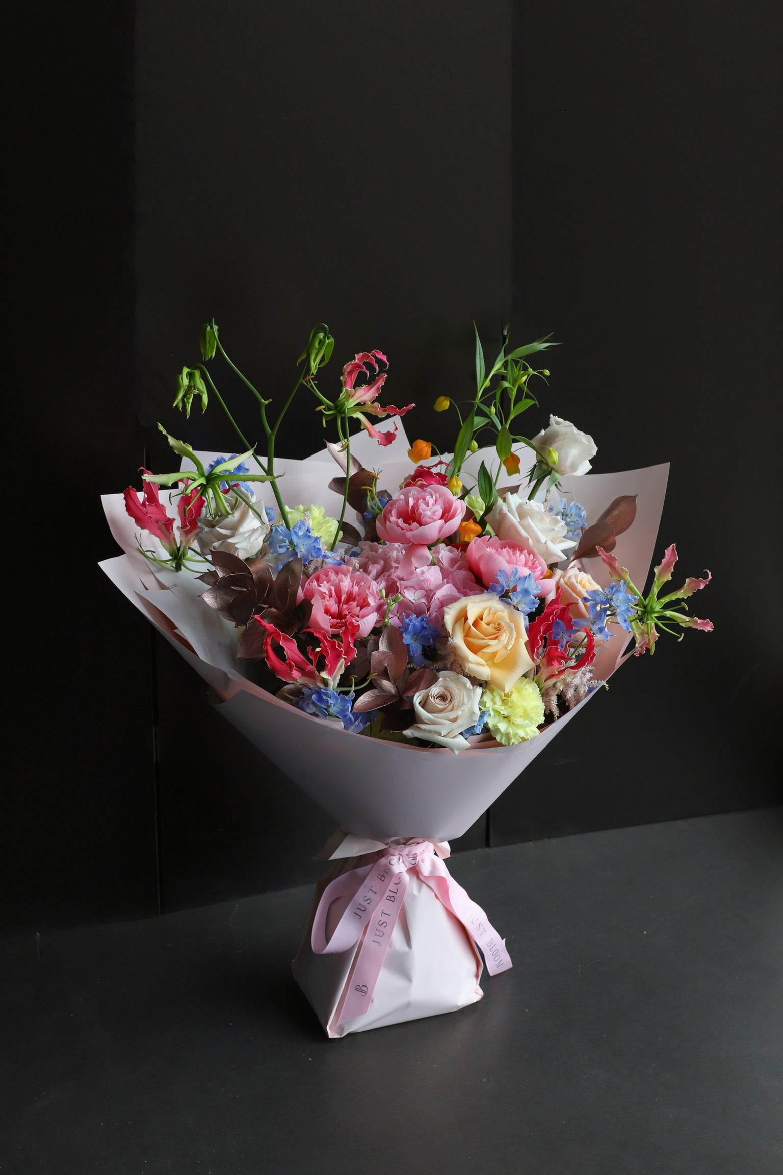 Wild Bunch luxury bouquet by Just Bloom Hong Kong featuring peonies, roses, delphiniums and flame lilies in blush and white wrapping with Just Bloom pink ribbon