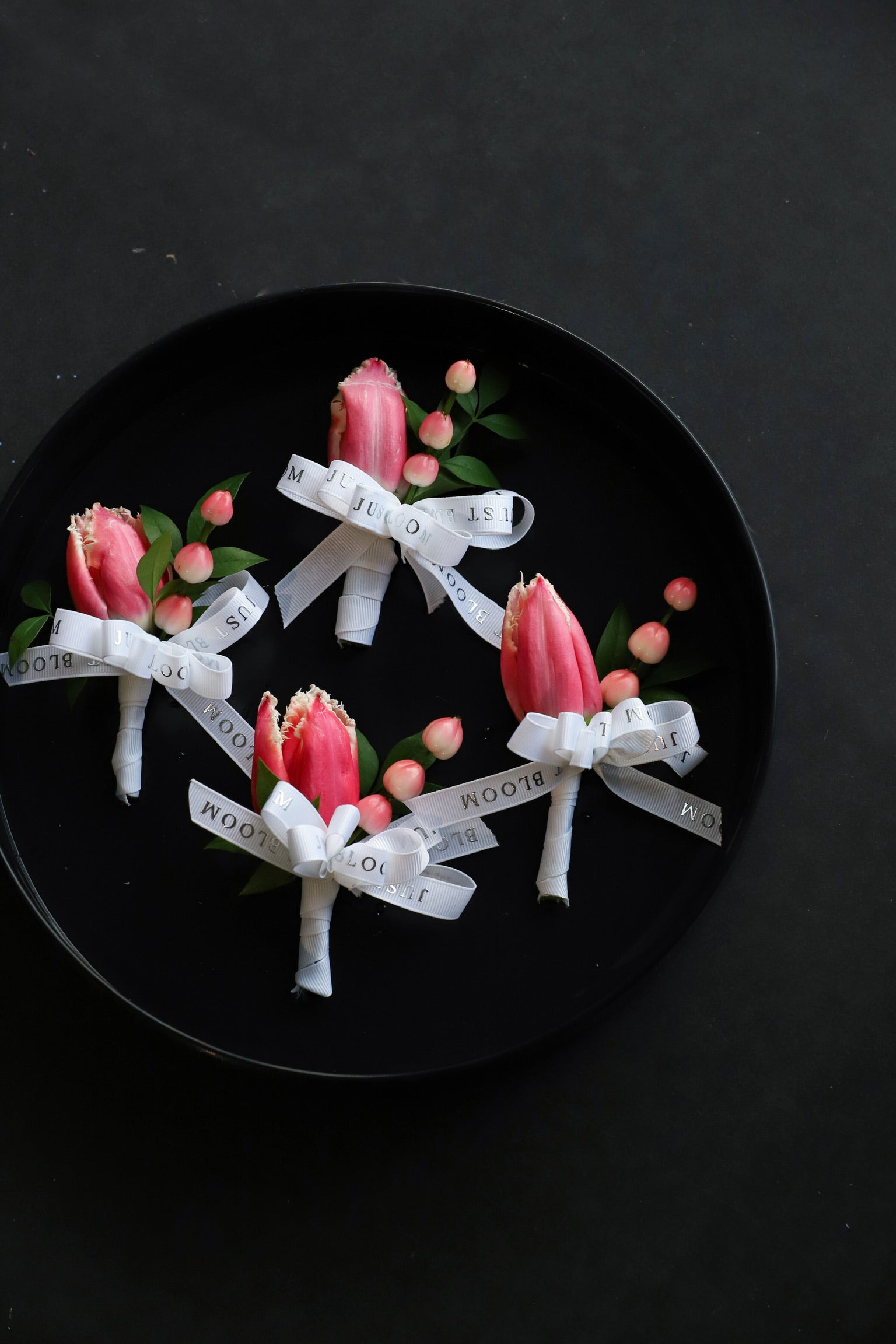 Close-up of four Boutonnieres on a black tray by Just Bloom Hong Kong, showcasing pink fringed tulips and hypericum berries with Just Bloom white ribbon
