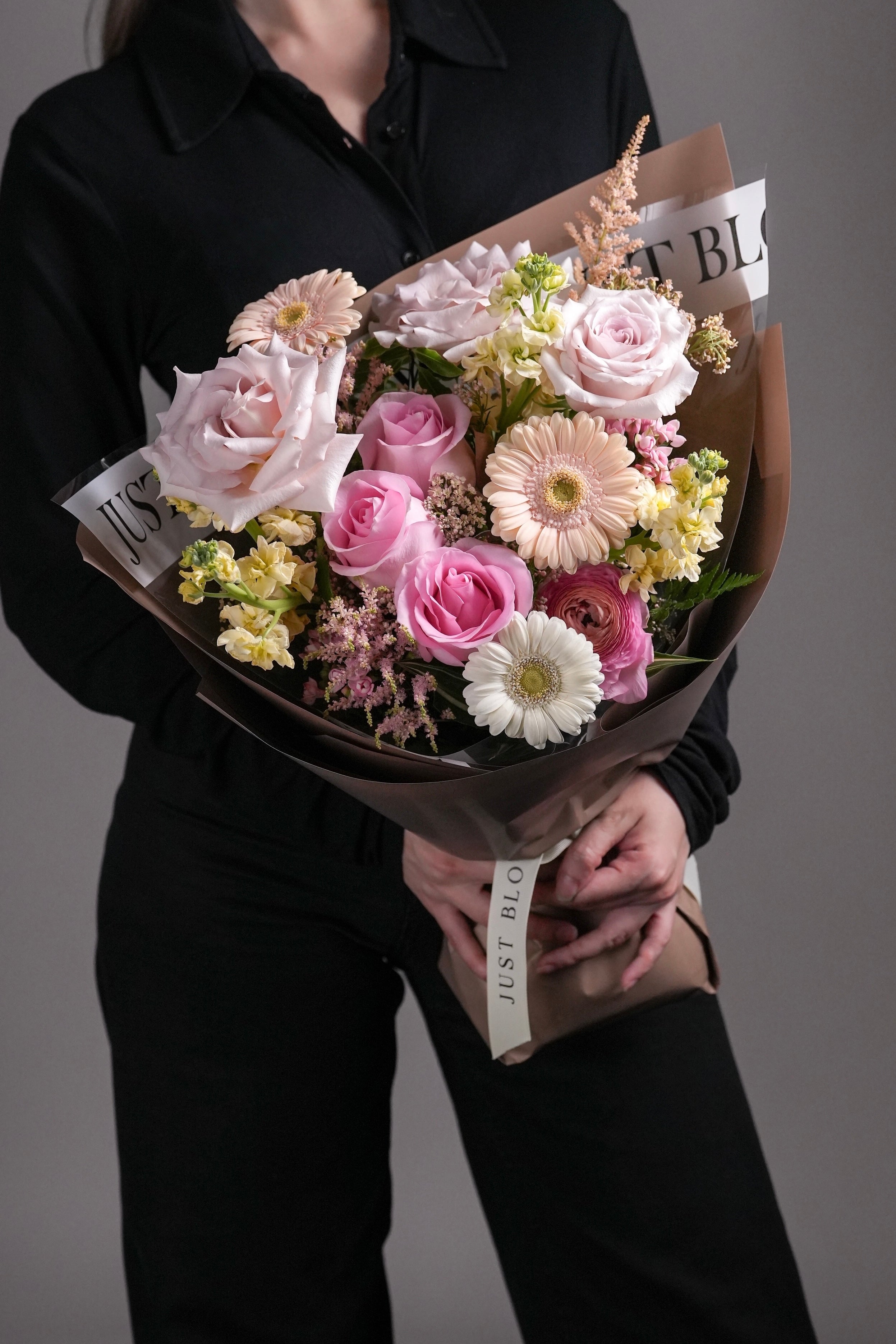 Model holding Asher bouquet with pink gerbera, yellow stock, and soft pink roses.