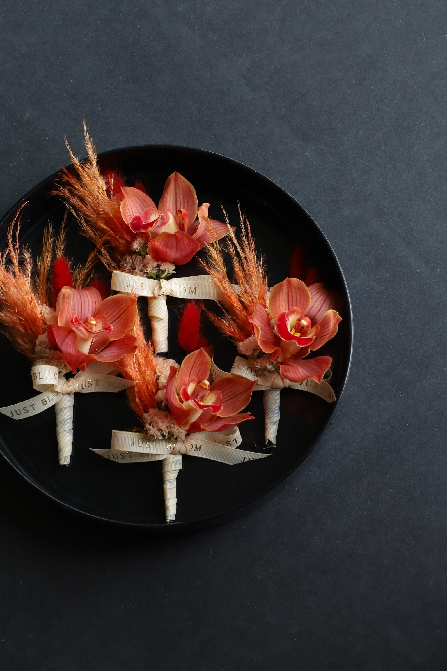 Four Bound Together corsages arranged on a black tray featuring cymbidium orchids, myosotis, dried lagurus ovatus and foliage tied with Just Bloom ivory ribbon — Just Bloom Hong Kong