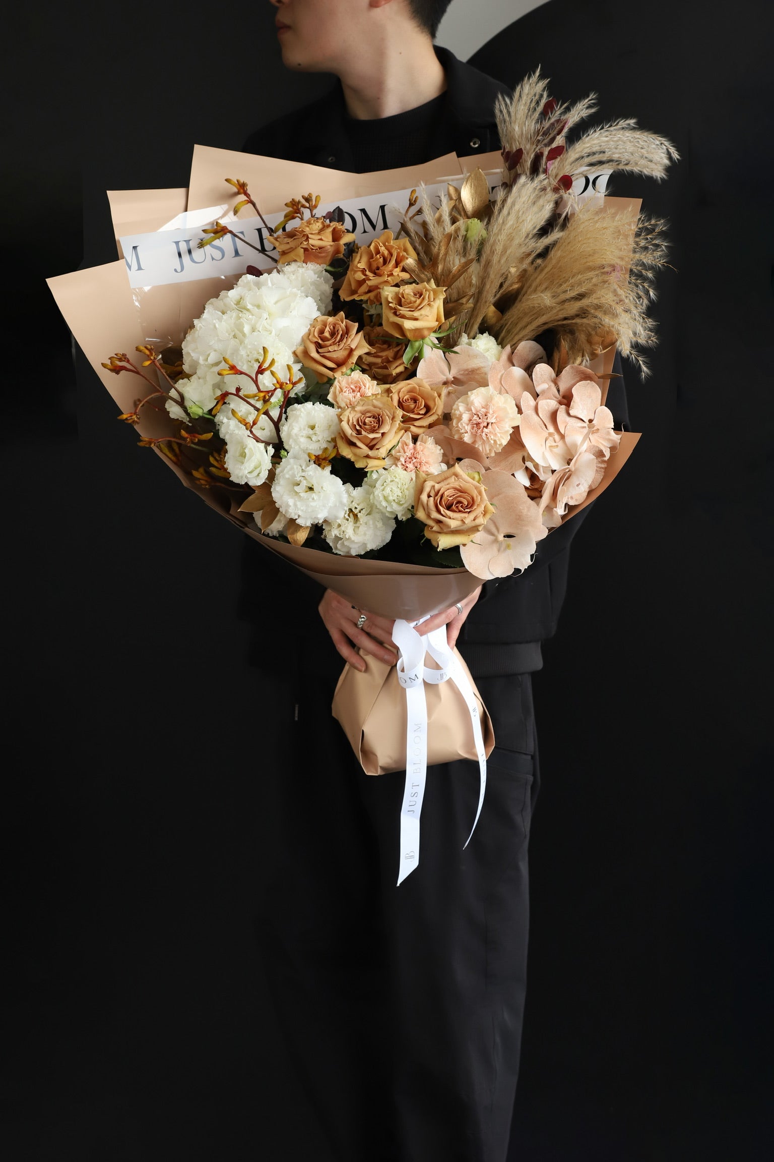 Model holding an oversized warm-toned fresh flower bouquet with toffee roses, white blooms, and dried elements wrapped in Just Bloom nude kraft paper — Just Bloom Hong Kong