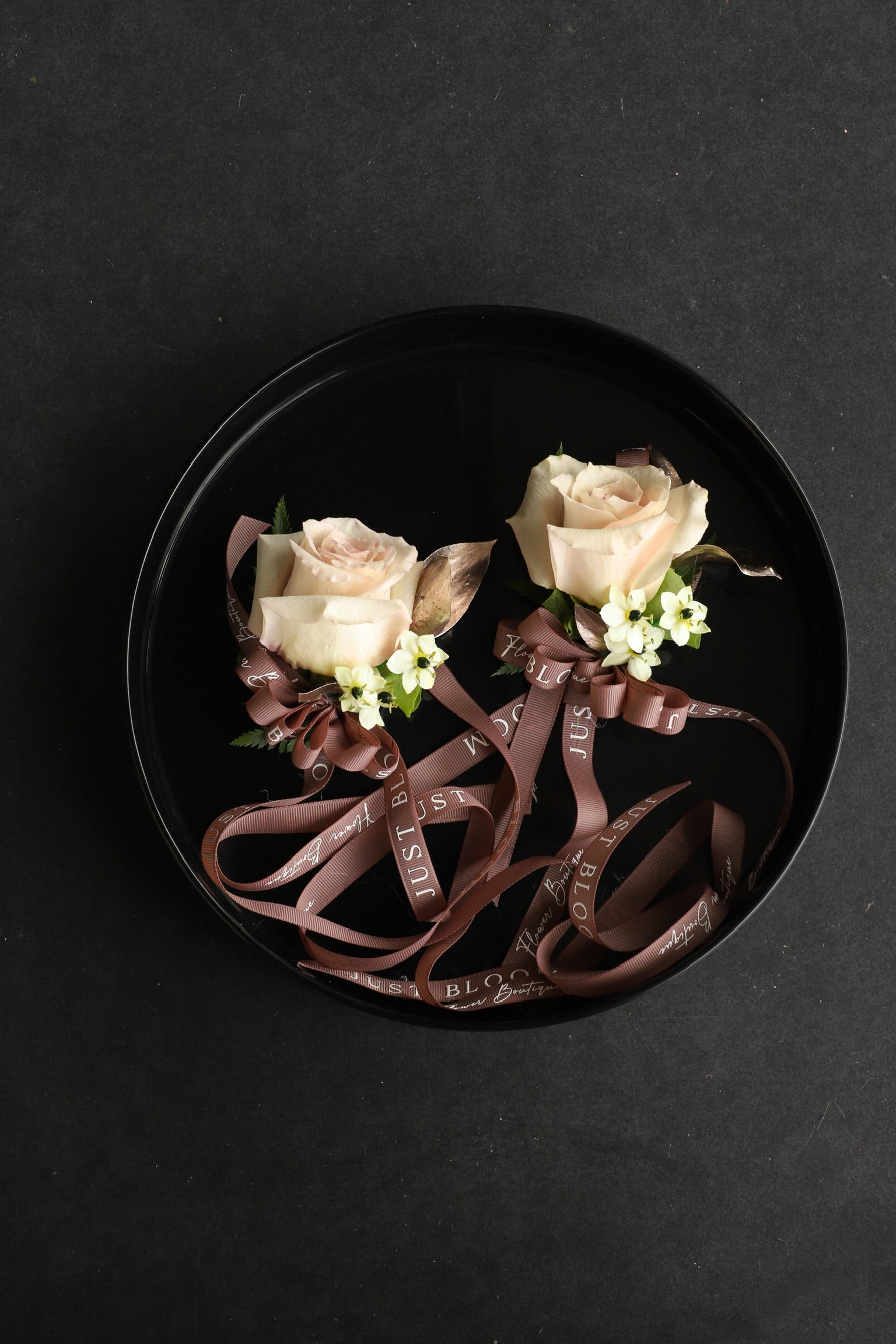 Two Wrist Corsage No.3 pieces arranged on a black tray featuring cream roses and star of Bethlehem with Just Bloom deep brown ribbon — Just Bloom Hong Kong