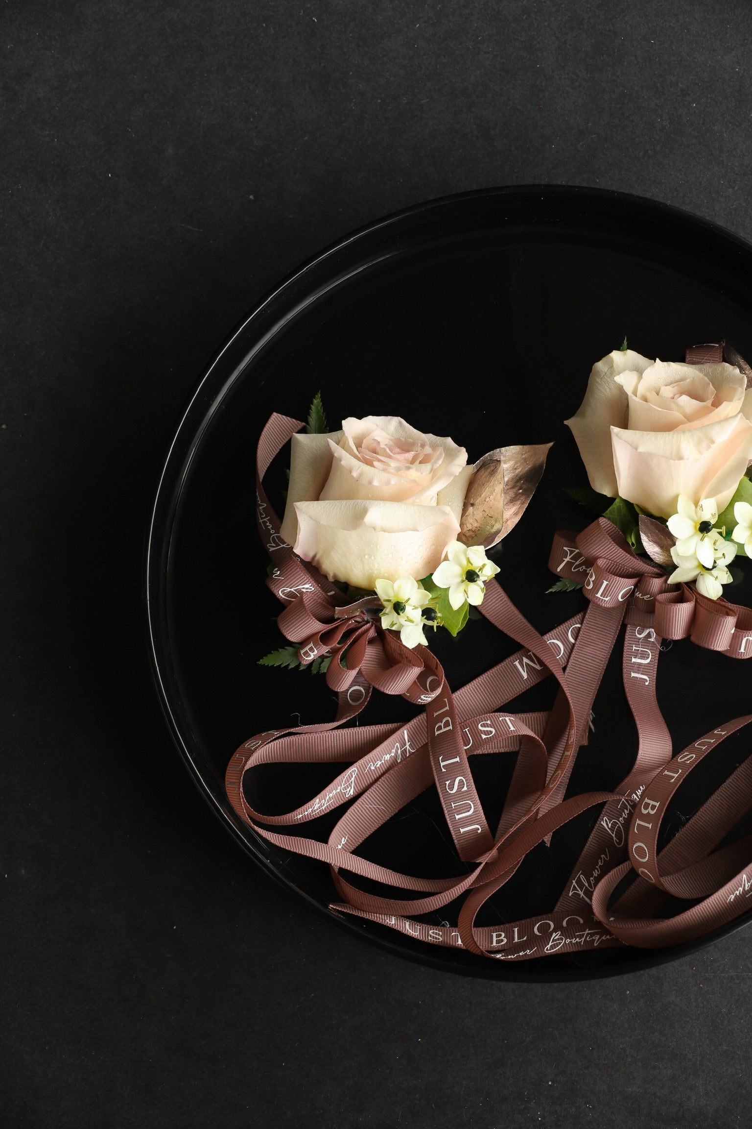 Close-up of two Wrist Corsage No.3 wedding wrist corsages on a black tray by Just Bloom Hong Kong, showcasing cream roses, star of Bethlehem and Just Bloom deep brown ribbon