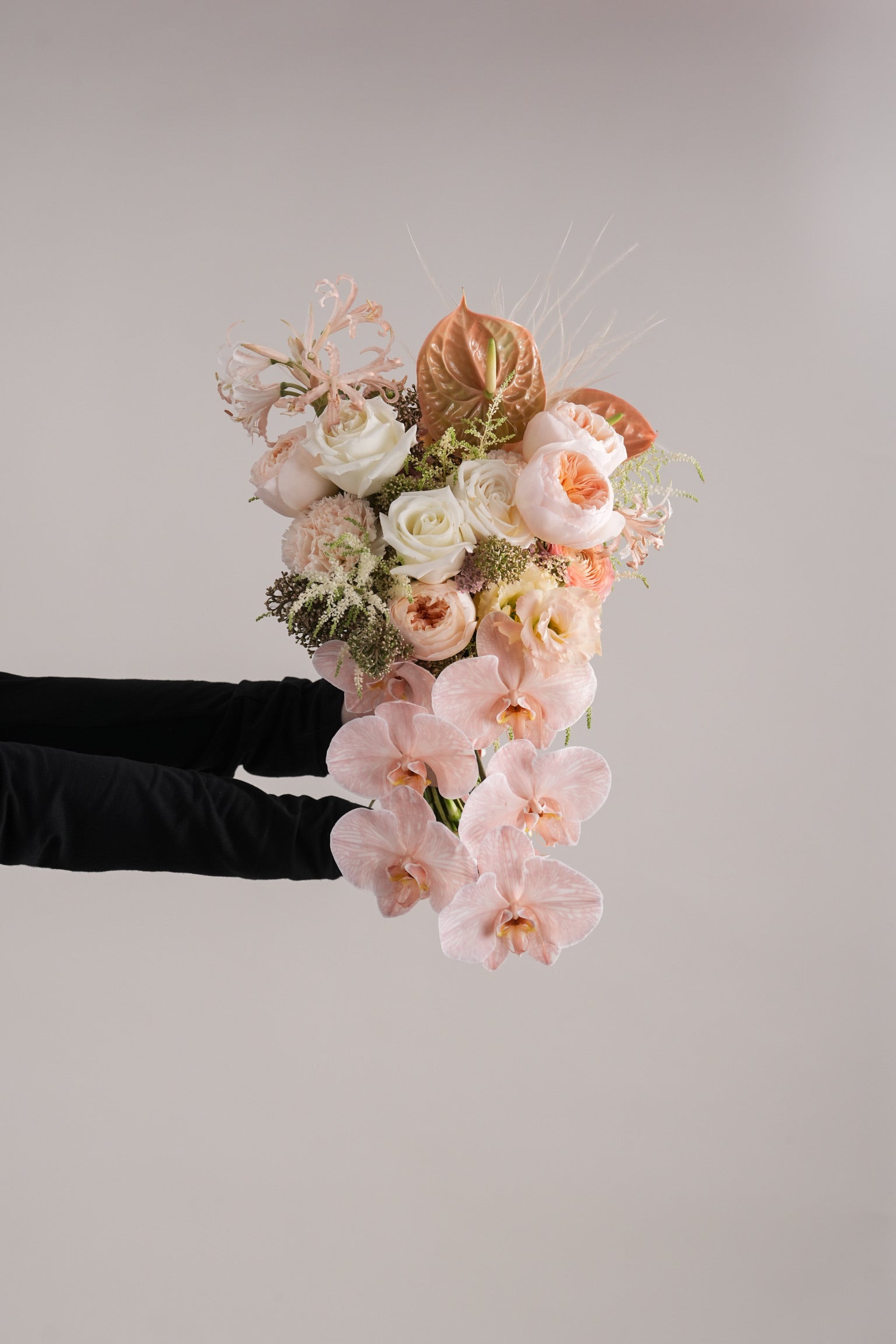 Close-up of Davina peach cascading bouquet held by hands, featuring orchids and roses