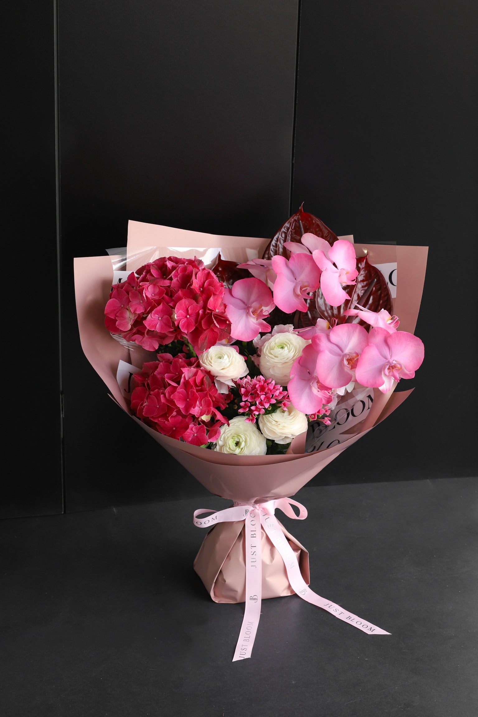 Large soft pink and peach fresh flower bouquet with sculptural blooms and silver foliage wrapped in white Just Bloom paper with pink ribbon against a dark background — Just Bloom Hong Kong