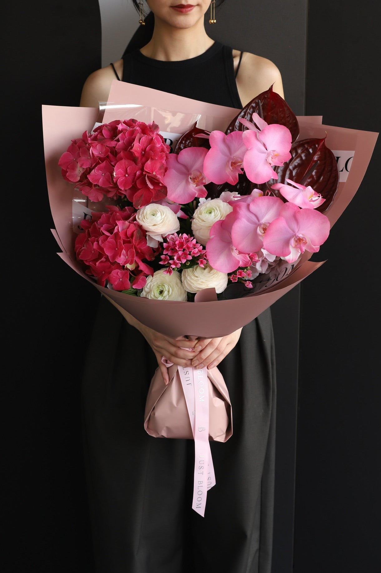 Model holding an oversized soft pink and peach fresh flower bouquet with roses, hydrangeas, and silver foliage wrapped in white Just Bloom paper with pink ribbon — Just Bloom Hong Kong
