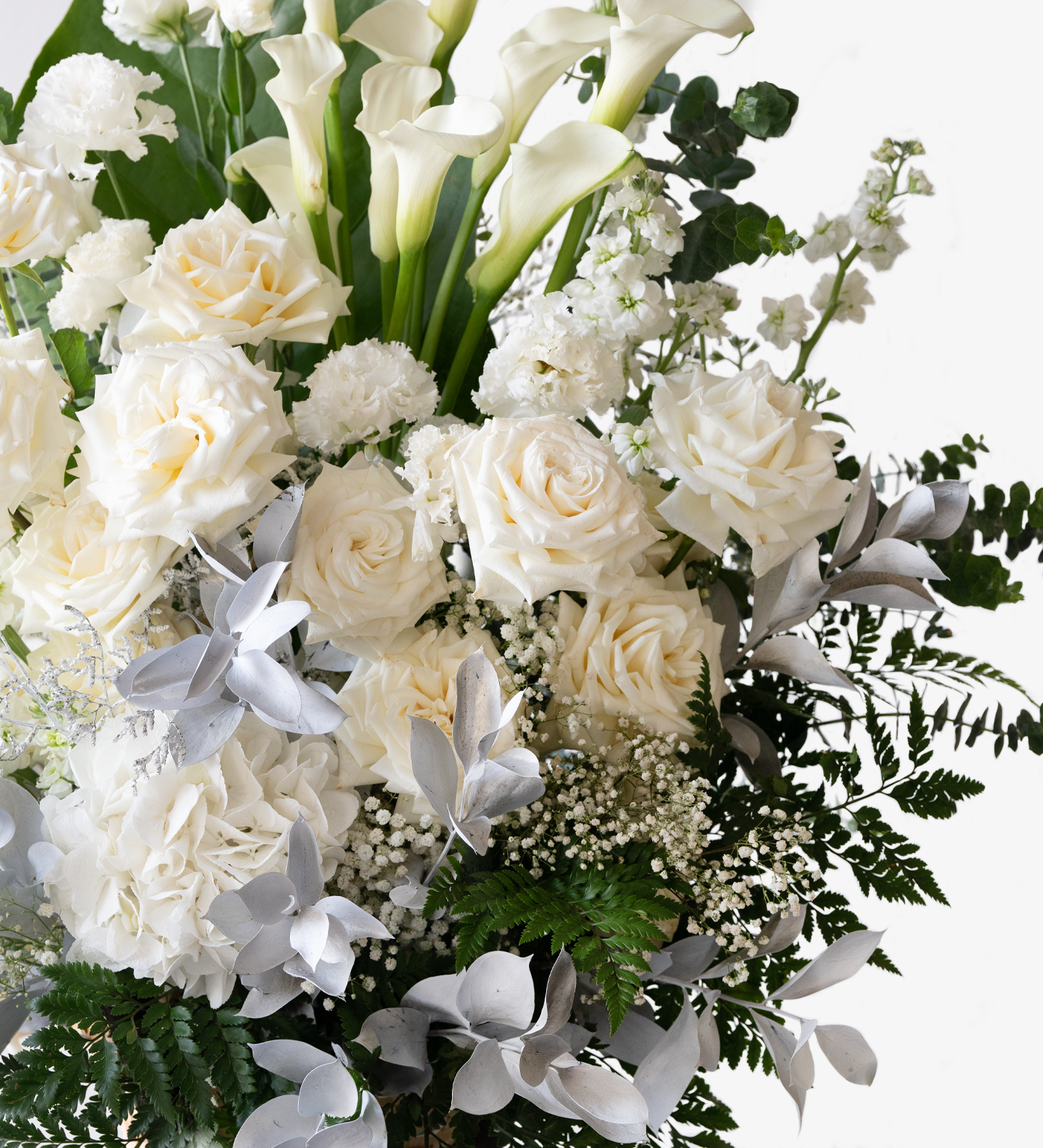 Close-up of roses, calla lilies, and baby’s breath in white condolence flower stand