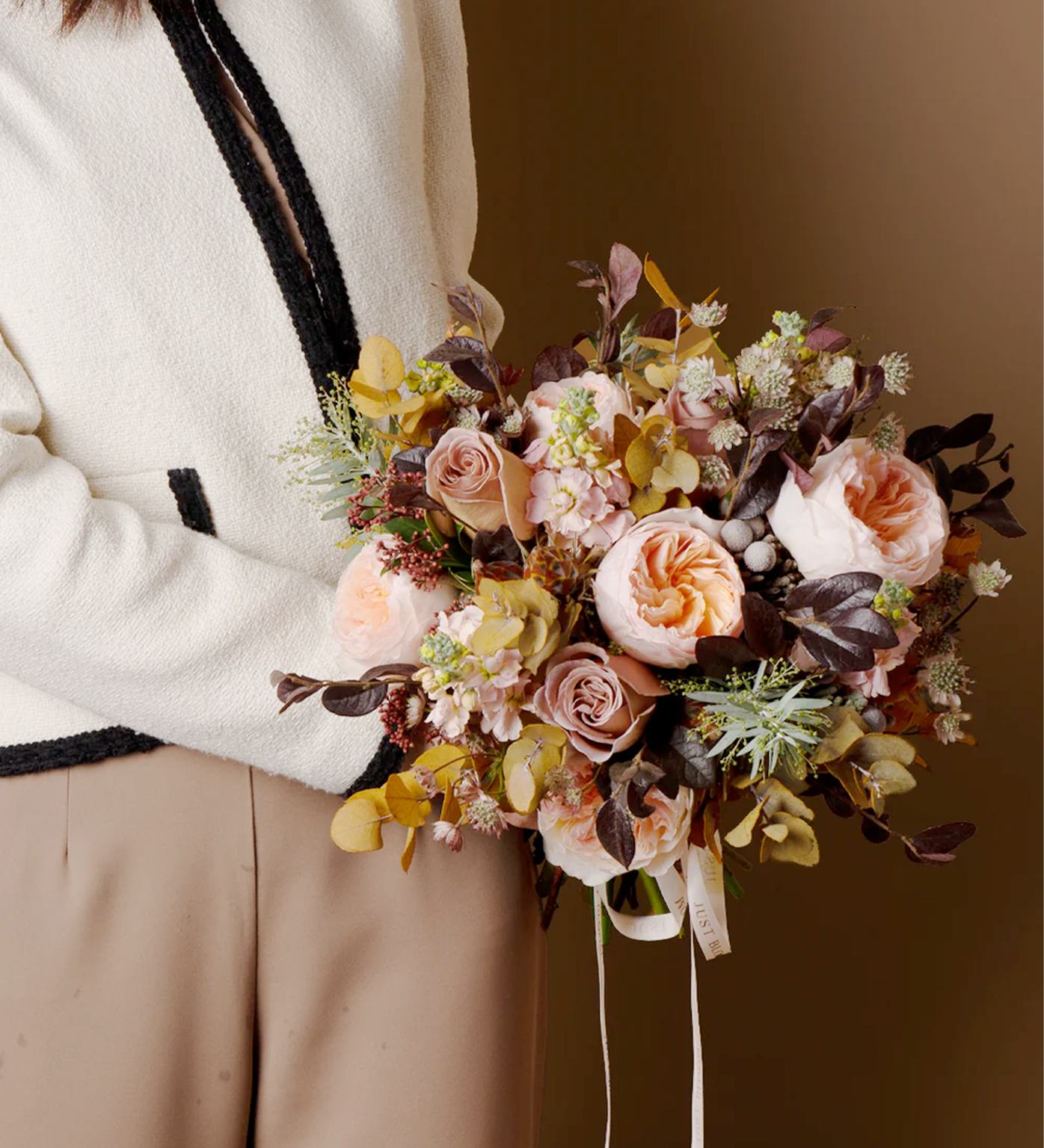 Woman holding Everly bridal bouquet with Ecuadorian garden roses and preserved leaves