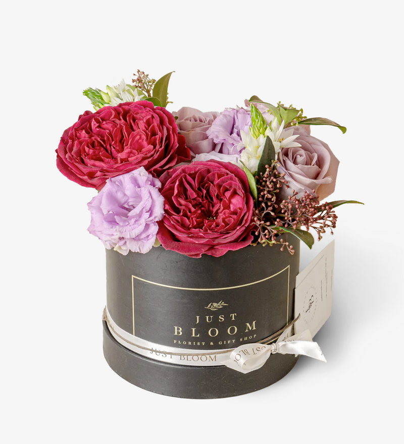An image of an exquisite Flower Box filled with premium Ecuadorian roses, David Austin Roses "Tess," and Dutch flower fillers, showcasing a harmonious blend of purple and burgundy tones, evoking a sense of romance and passion.