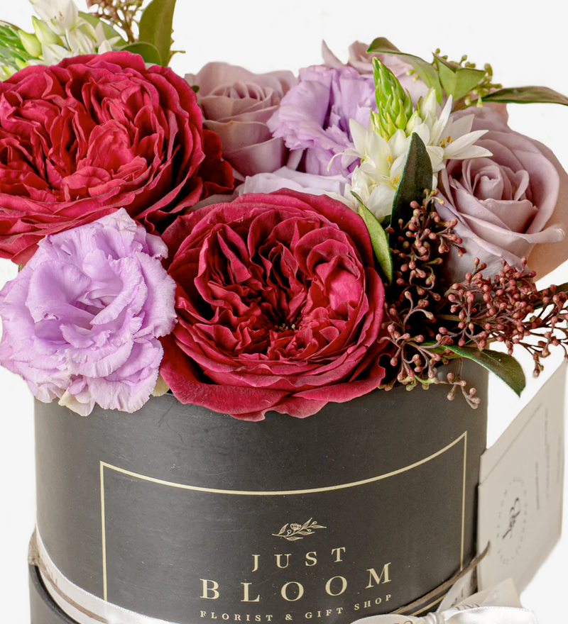 An image of an exquisite Flower Box filled with premium Ecuadorian roses, David Austin Roses "Tess," and Dutch flower fillers, showcasing a harmonious blend of purple and burgundy tones, evoking a sense of romance and passion.
