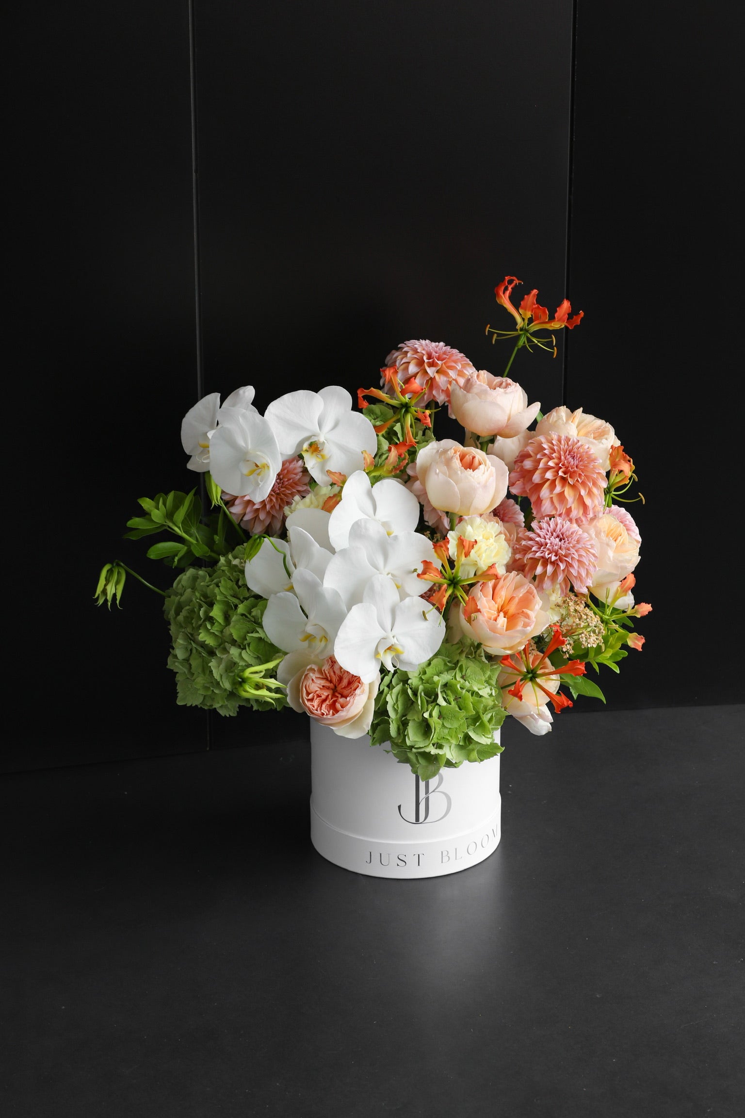 Luxurious peach and white flower box arrangement with Phalaenopsis Orchids, Garden Roses, Dahlias, and Gloriosa in a white Just Bloom hat box against a dark background — Just Bloom Hong Kong