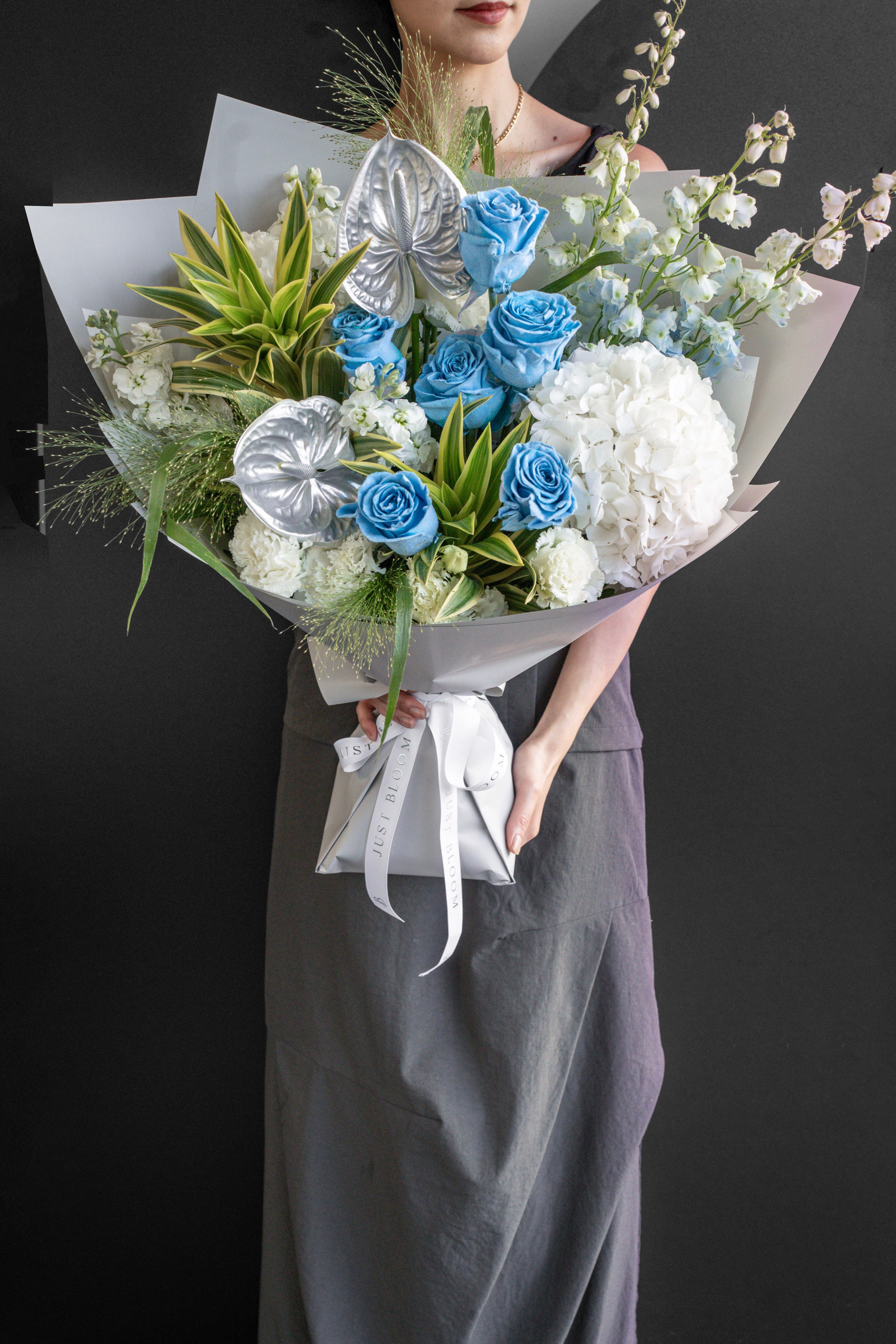 Model holding the Frost Bloom bouquet of blue roses and white hydrangea against a black backdrop — Just Bloom Hong Kong