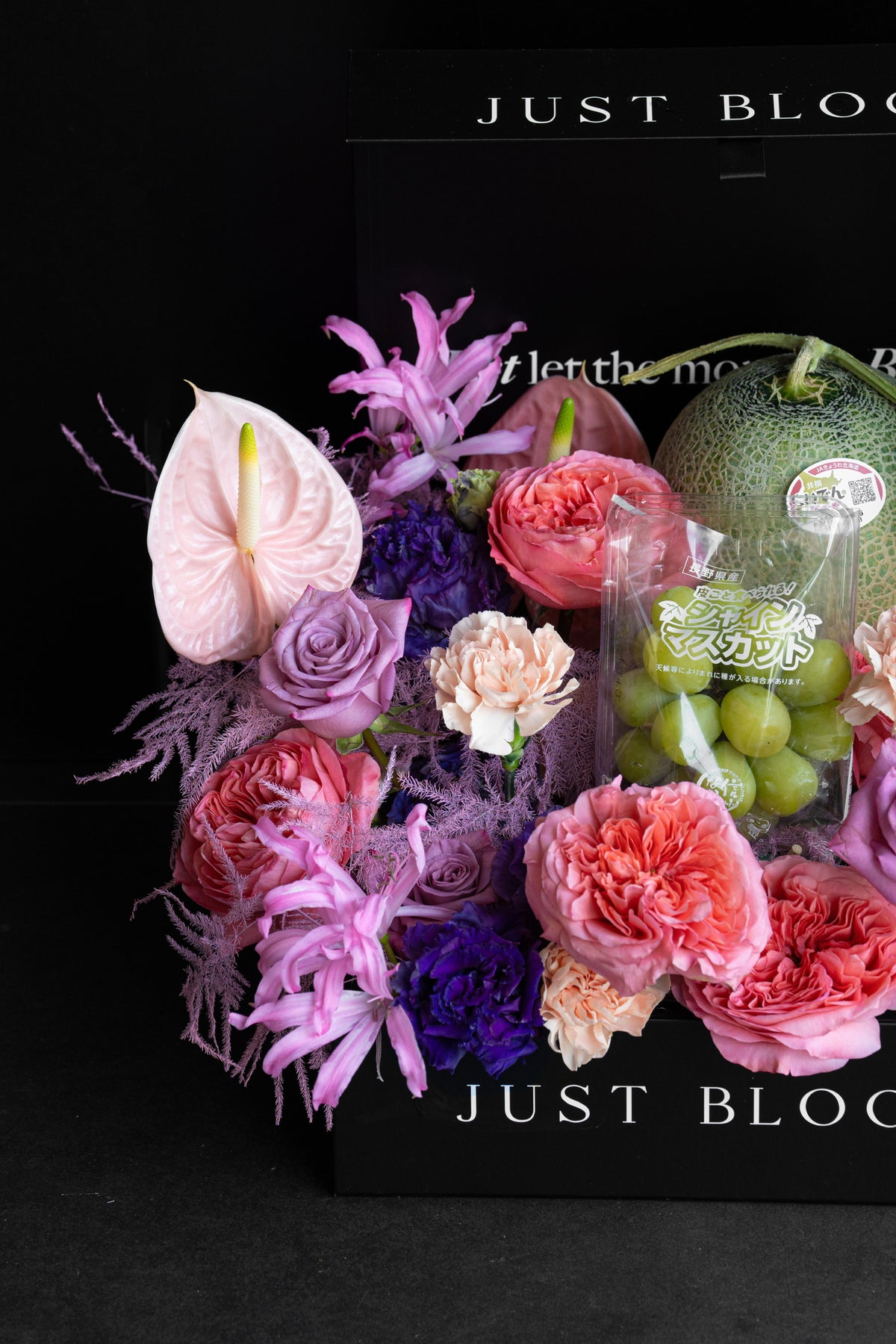 Side angle of Blush Altar hamper showing the full layered floral arrangement in pink, lavender, and violet tones with premium fruits nestled in the gift box