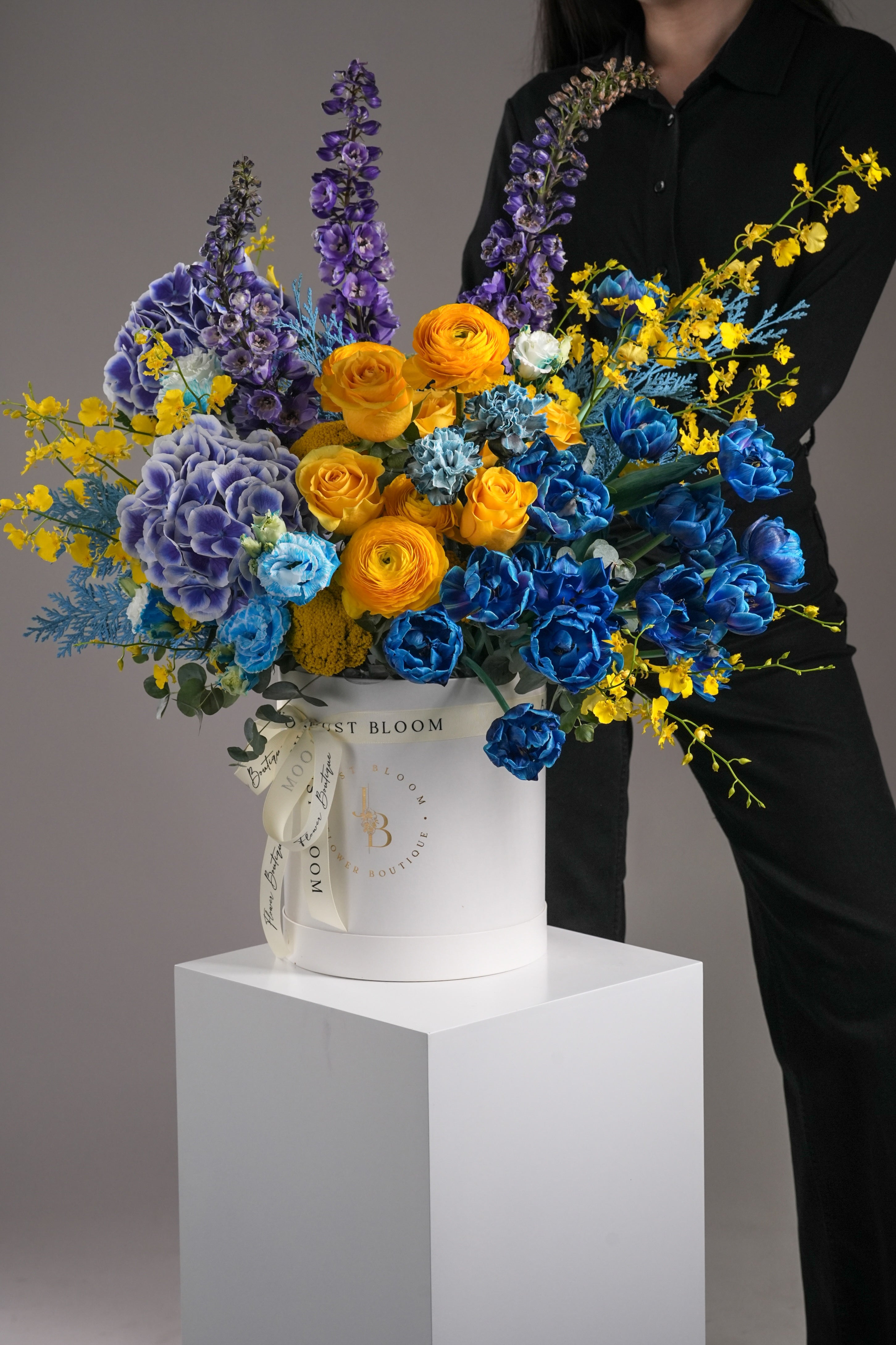 Just Bloom Hong Kong Arlo fresh flower box – lifestyle image showing a model standing behind a vivid blue and gold flower box in a modern studio setting
