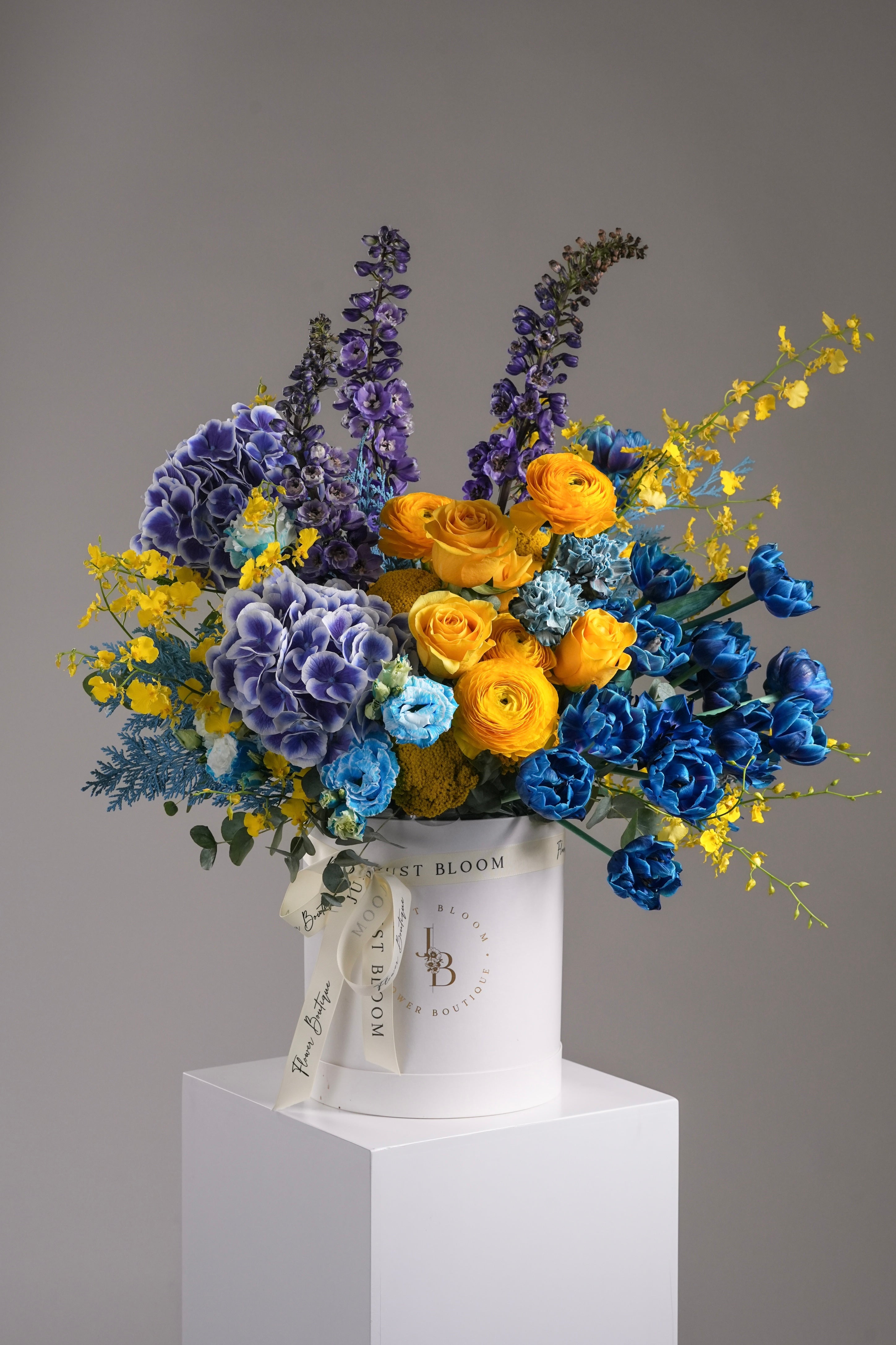 Just Bloom Hong Kong Arlo fresh flower box – studio image showing a large luxury blue and yellow floral arrangement in a white round hatbox, placed on a pedestal