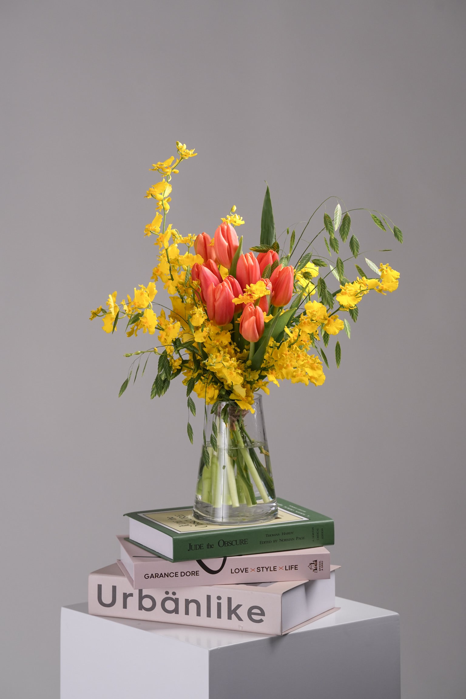 Katalina spring vase arrangement with coral tulips and golden mimosa on stacked design books – full composition view