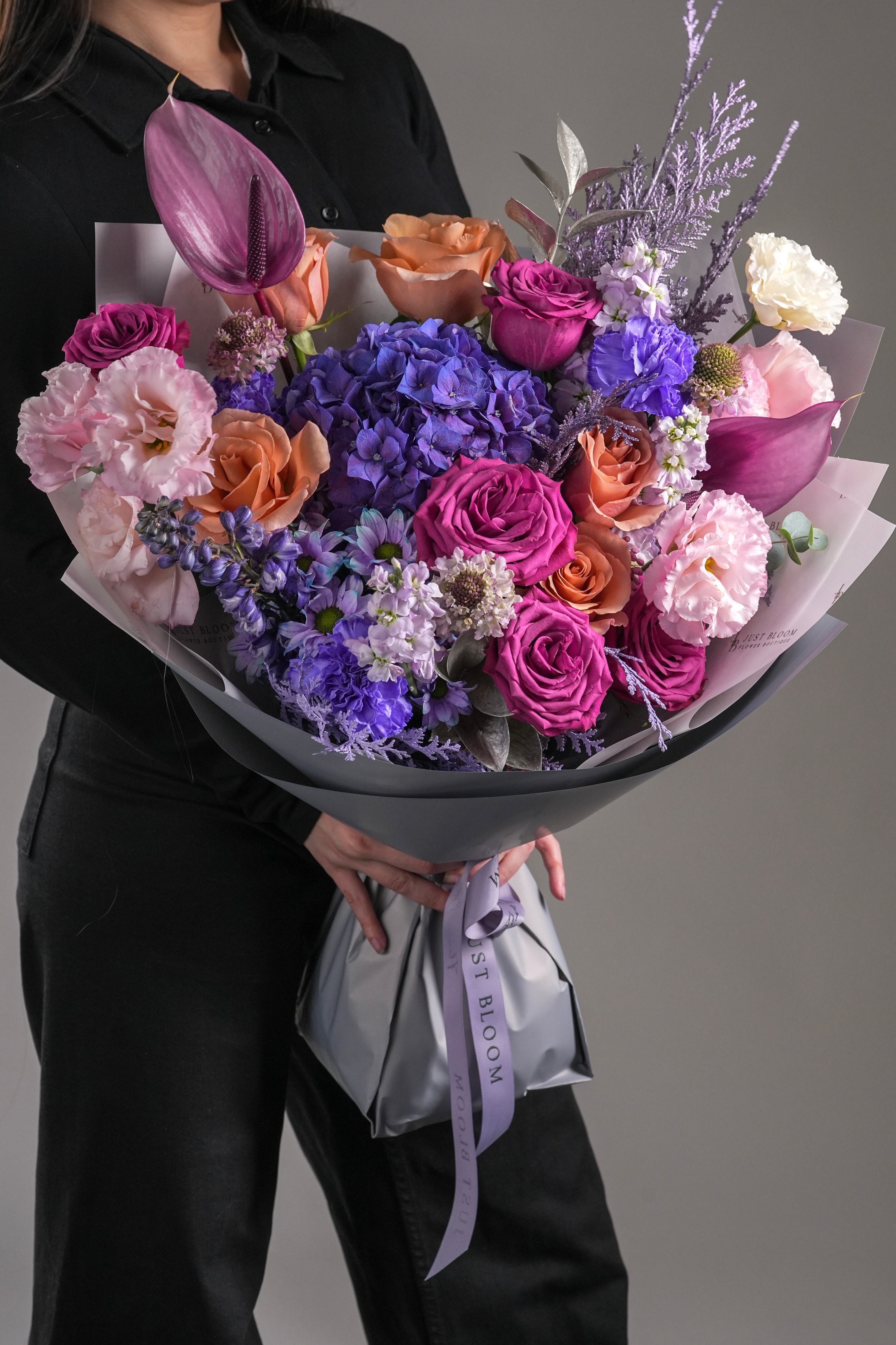 Kaylee purple hydrangea and mixed rose bouquet held by woman in black shirt with grey wrapping