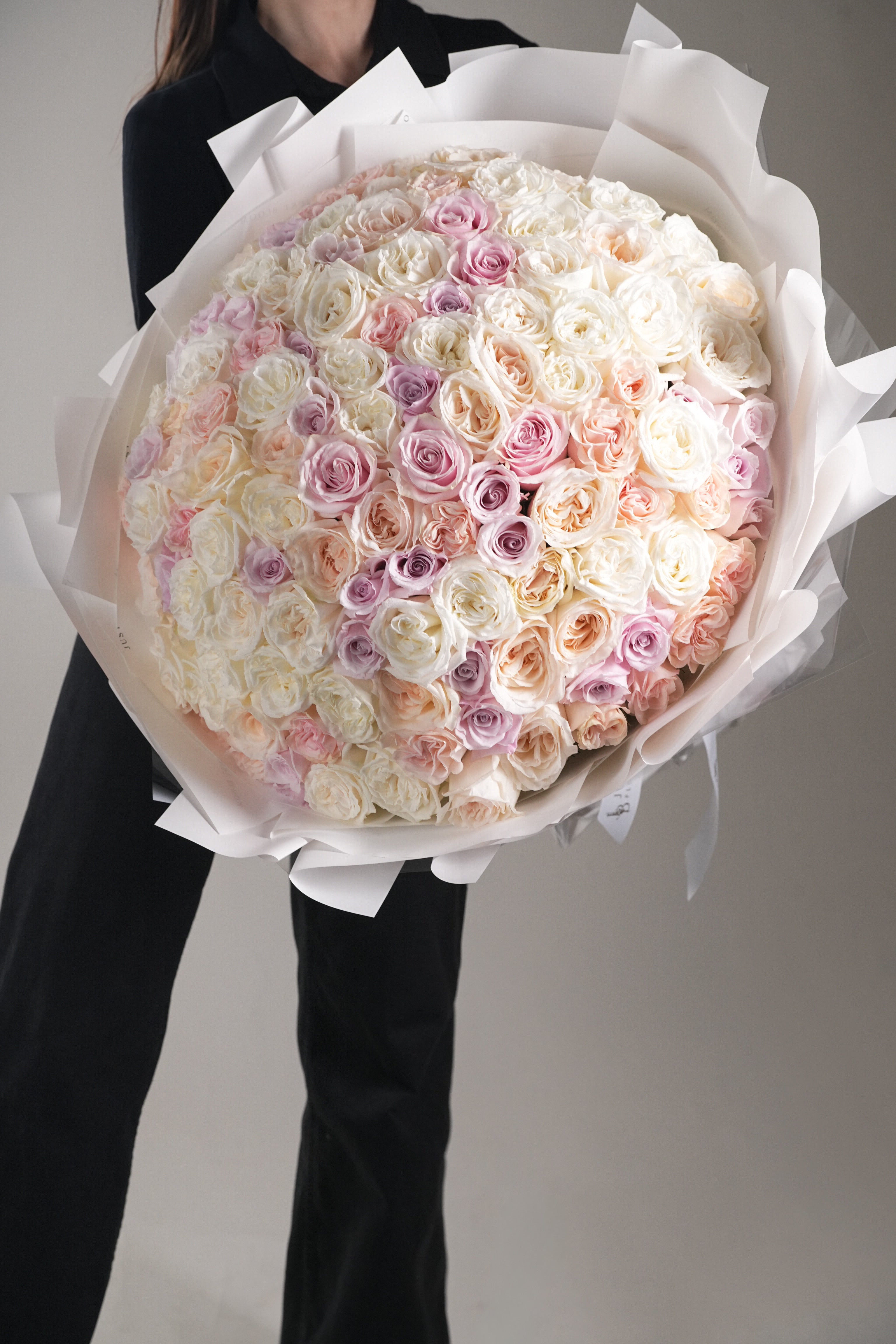 Kelly luxury large premium rose bouquet in white and pastel tones held by woman in black outfit
