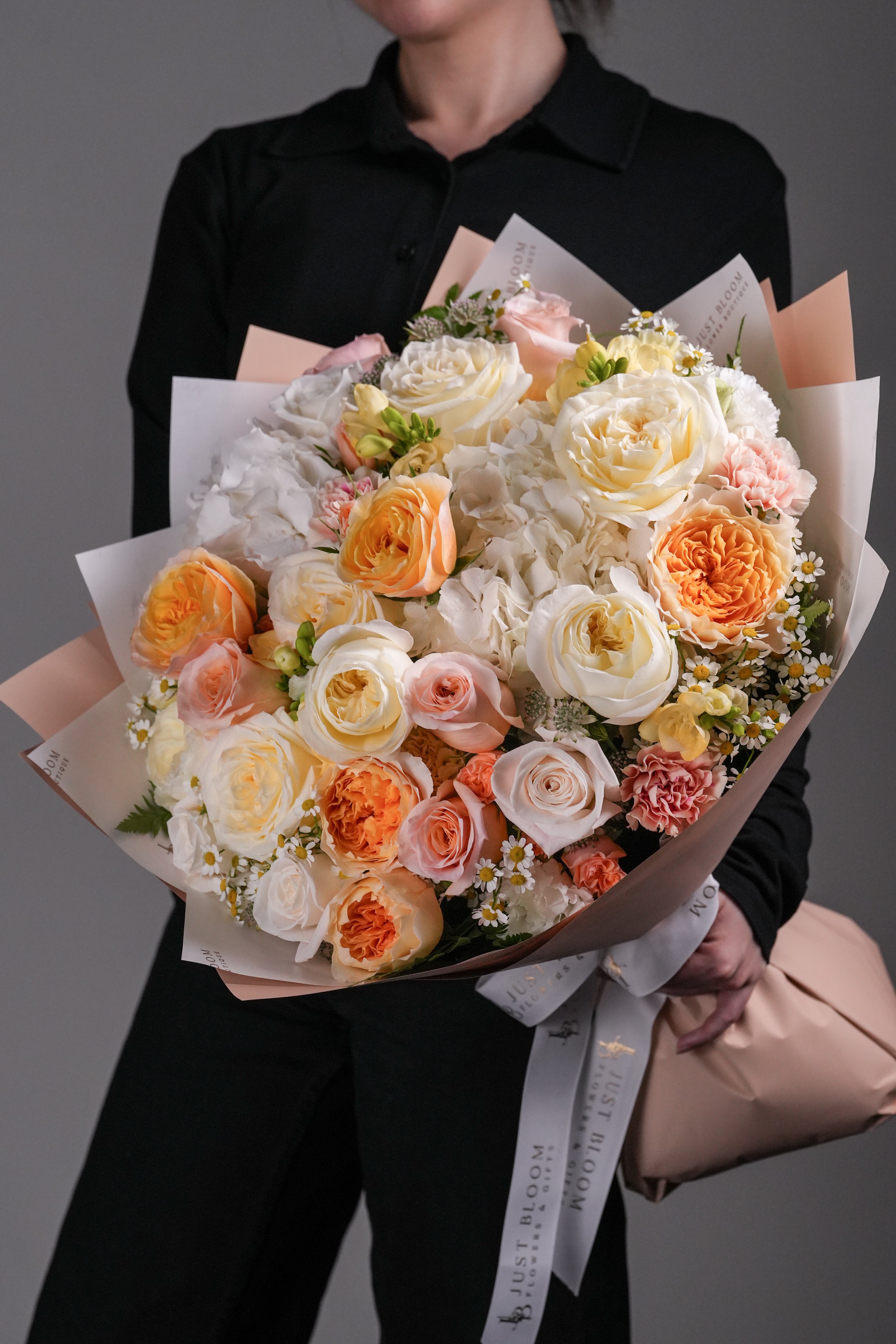 Khloe garden rose and hydrangea mixed bouquet in peach and cream tones held by woman in black outfit