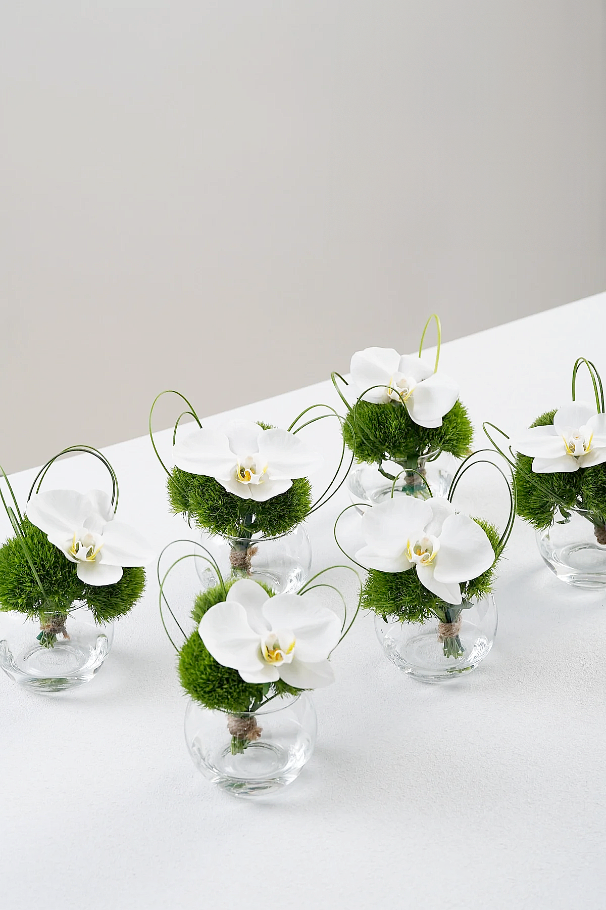 Multiple Laney mini vase arrangements showing white orchids and curved lily grass in modern styling