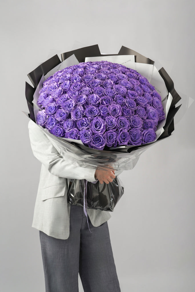 Lavender ultra-luxury purple rose bouquet with dozens of Ecuadorian roses in black and white wrapping held by person