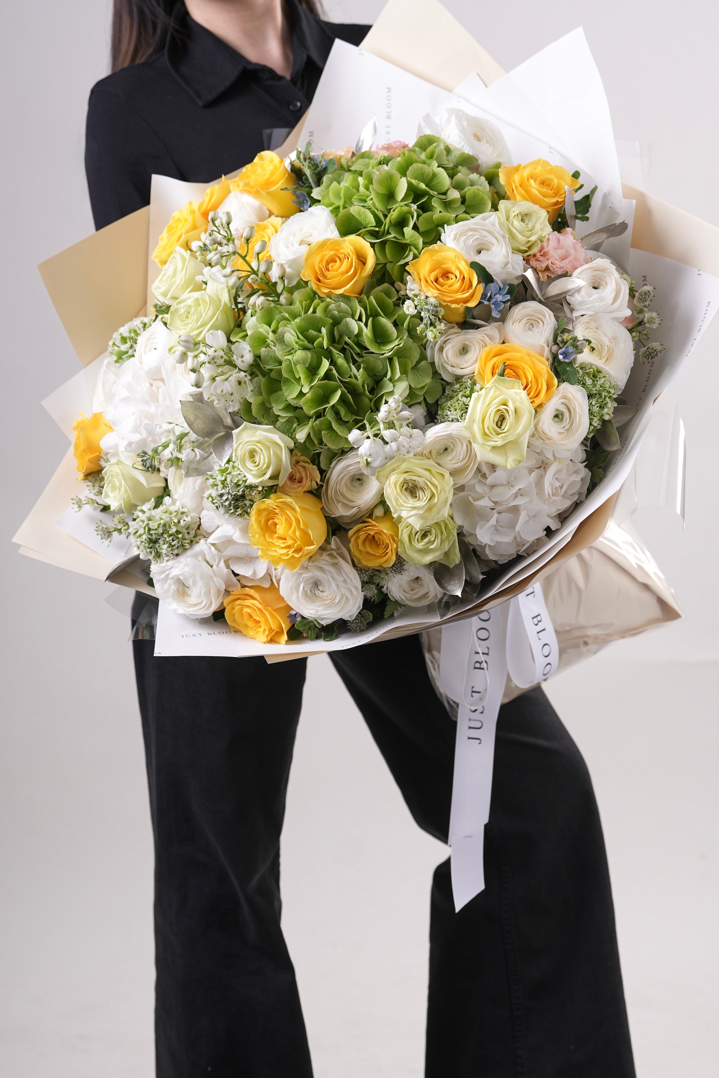Lilly large yellow and green mixed flower bouquet held by woman in black outfit with champagne wrapping