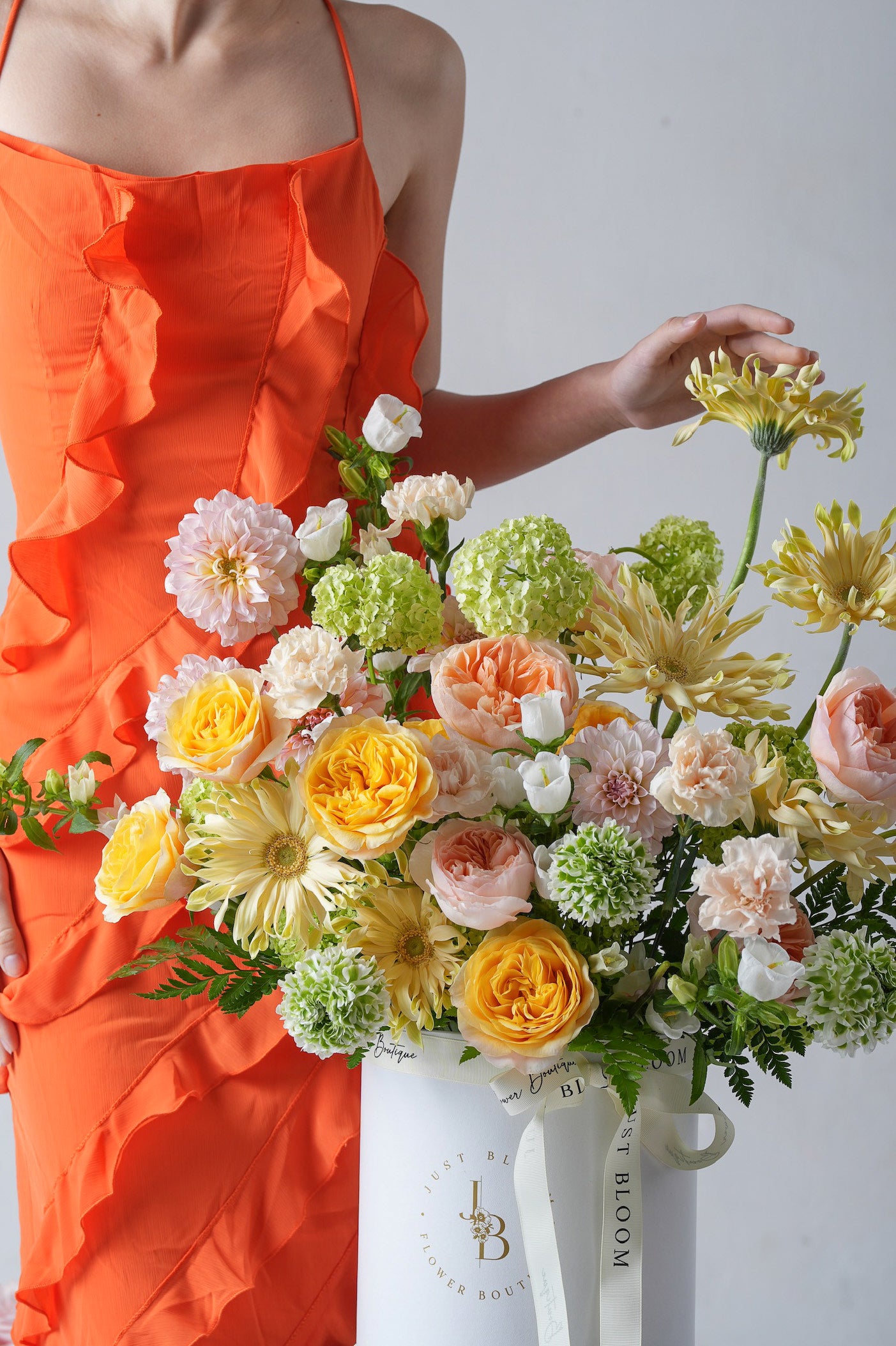A radiant hatbox arrangement with yellow garden roses, peach ranunculus, and creamy carnations tied with a satin ribbon.