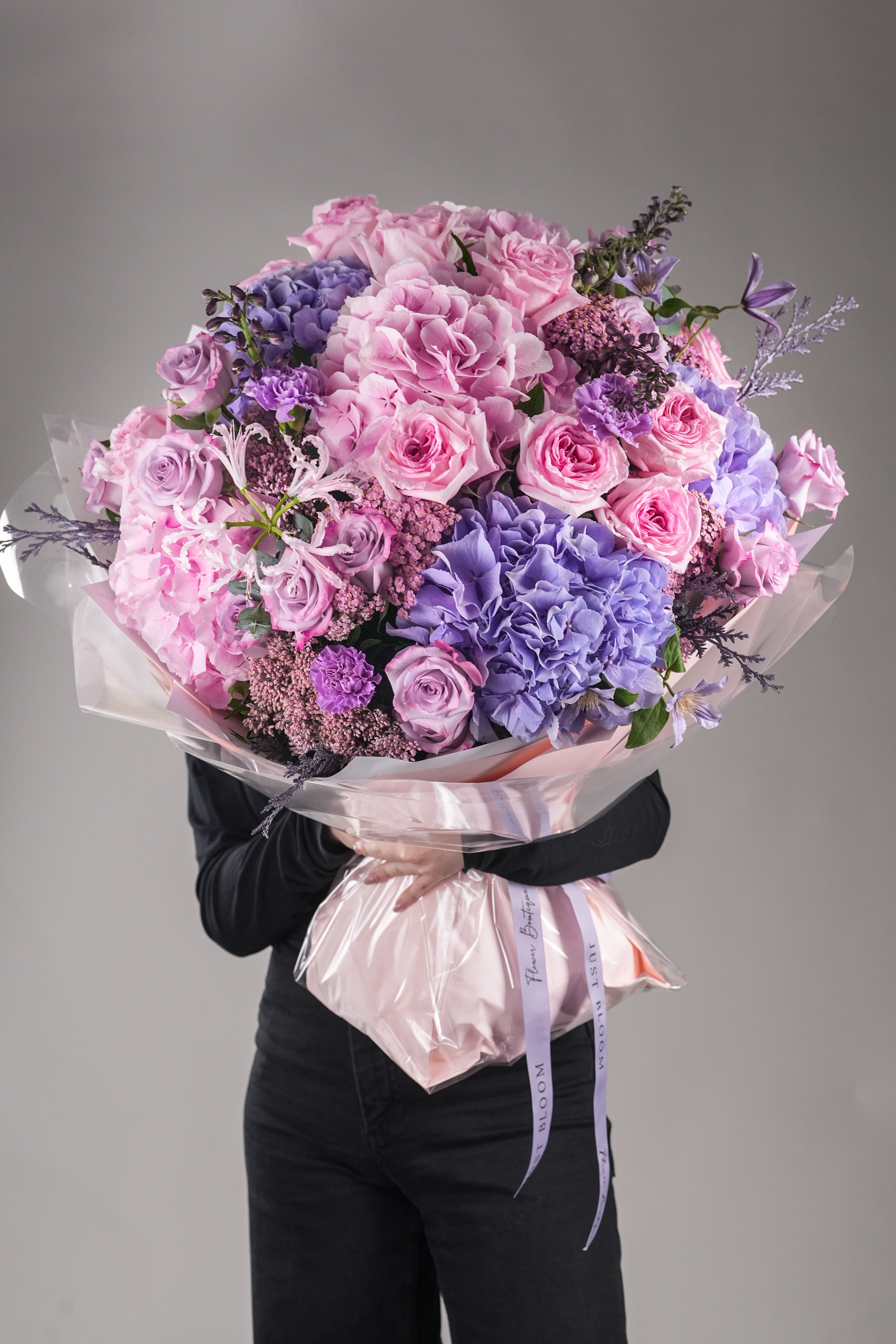 Livia dreamy pink and purple large garden rose bouquet held by woman in black outfit with clear wrapping