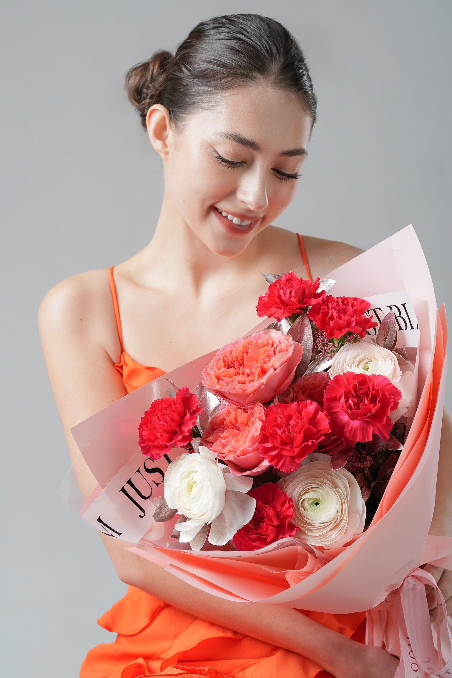 A vibrant bouquet with red carnations, peach roses, and white ranunculus wrapped