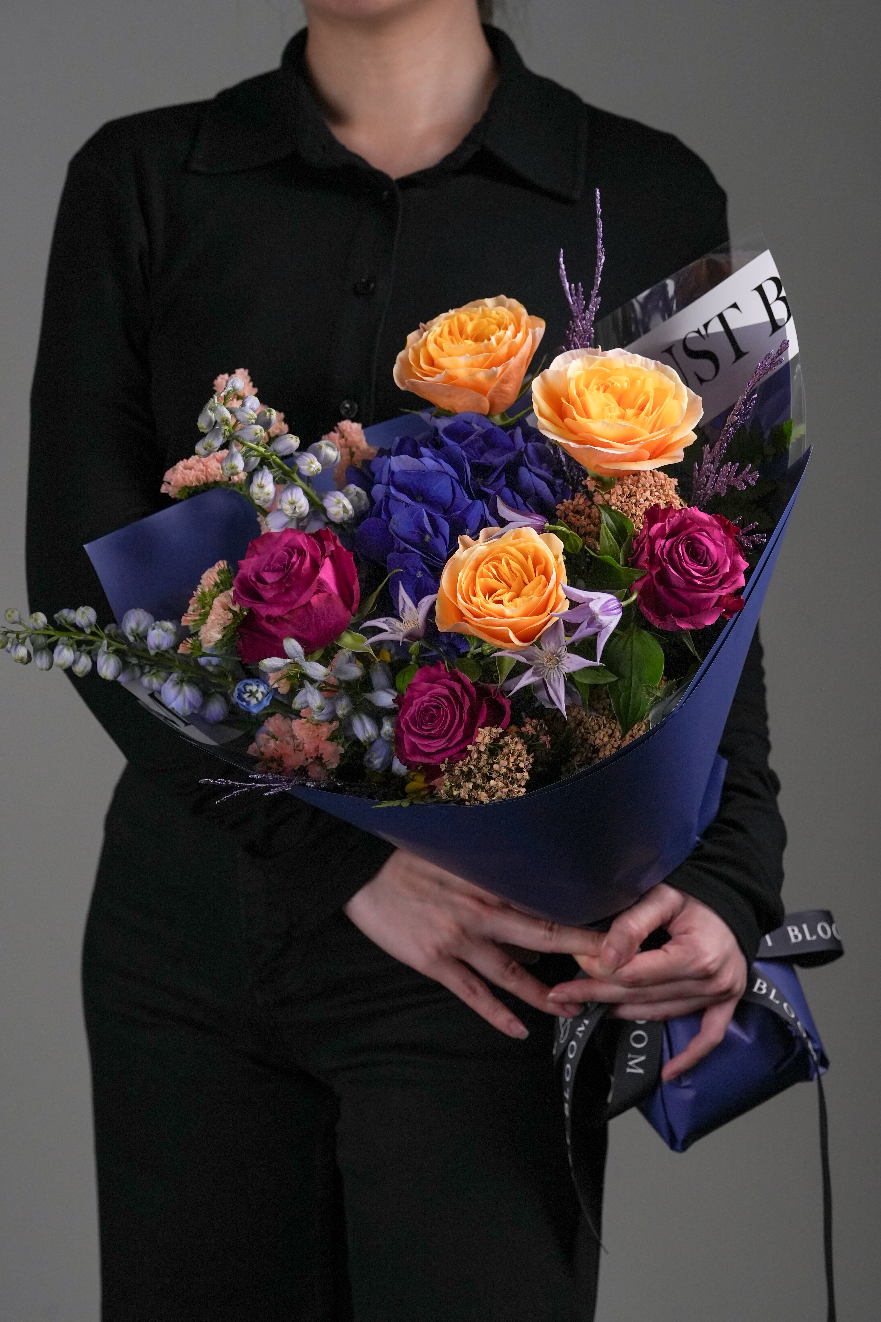 Lucas bold orange and blue mixed rose bouquet held by woman in black outfit with navy wrapping