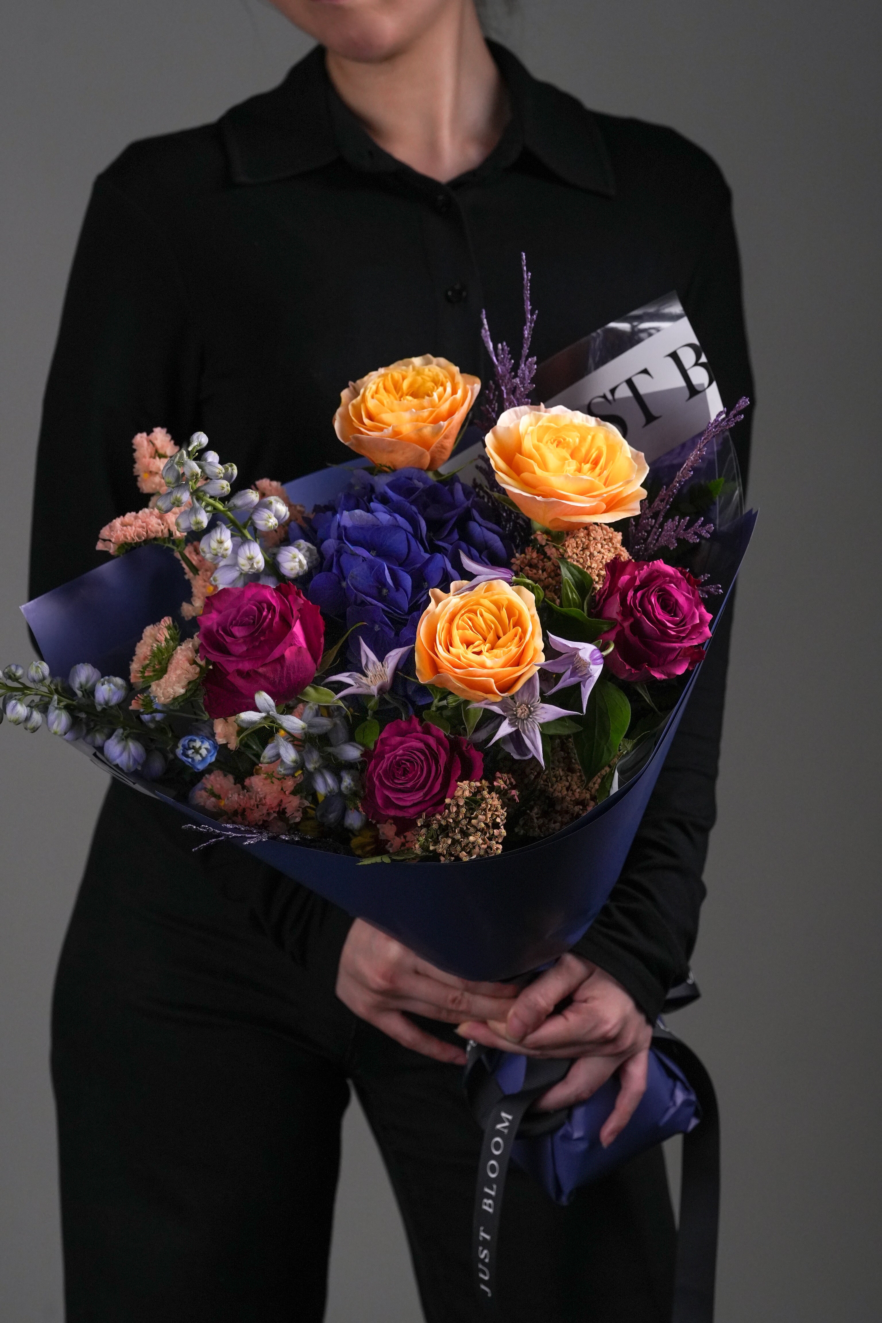 Close-up view of Lucas bouquet showing orange roses, blue hydrangeas, and purple delphinium arrangement