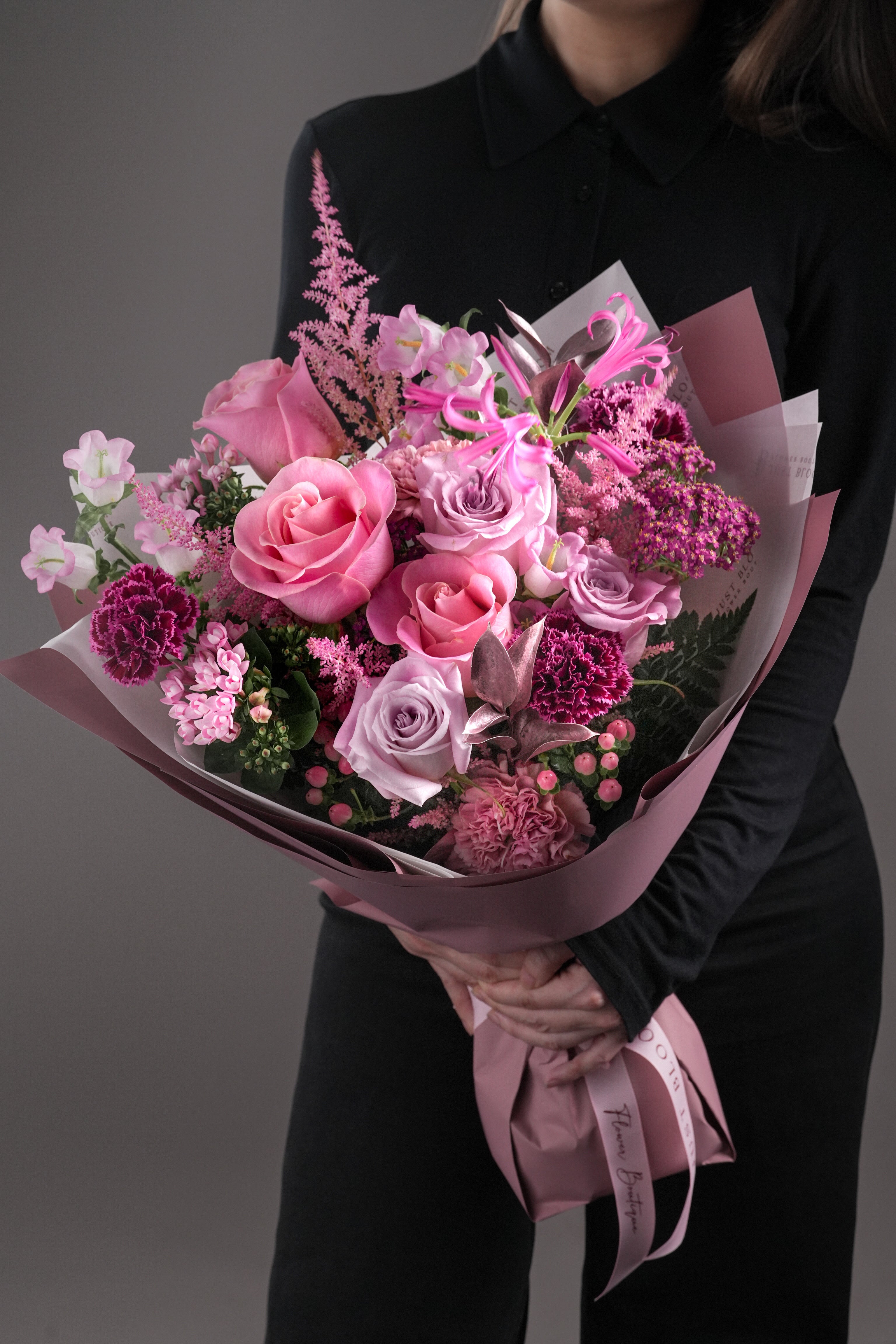 Lucy pretty in pink rose and carnation bouquet held by woman in black shirt with coordinating pink wrapping