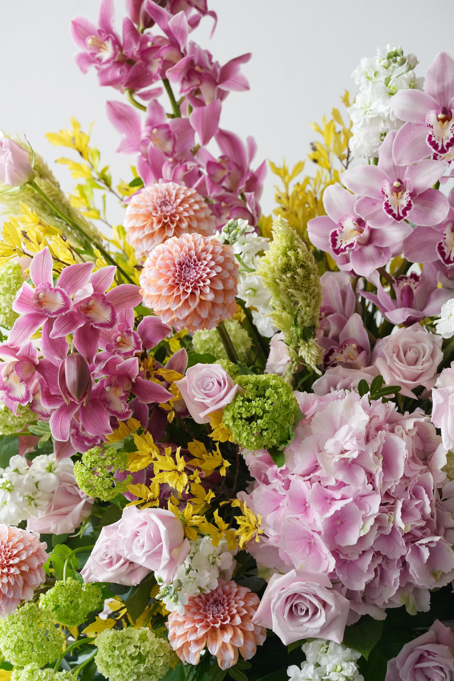 Close-up of Marseille flower stand showing cymbidium orchids, dahlias, lavender roses, hydrangeas, viburnum, and yellow accent flowers 