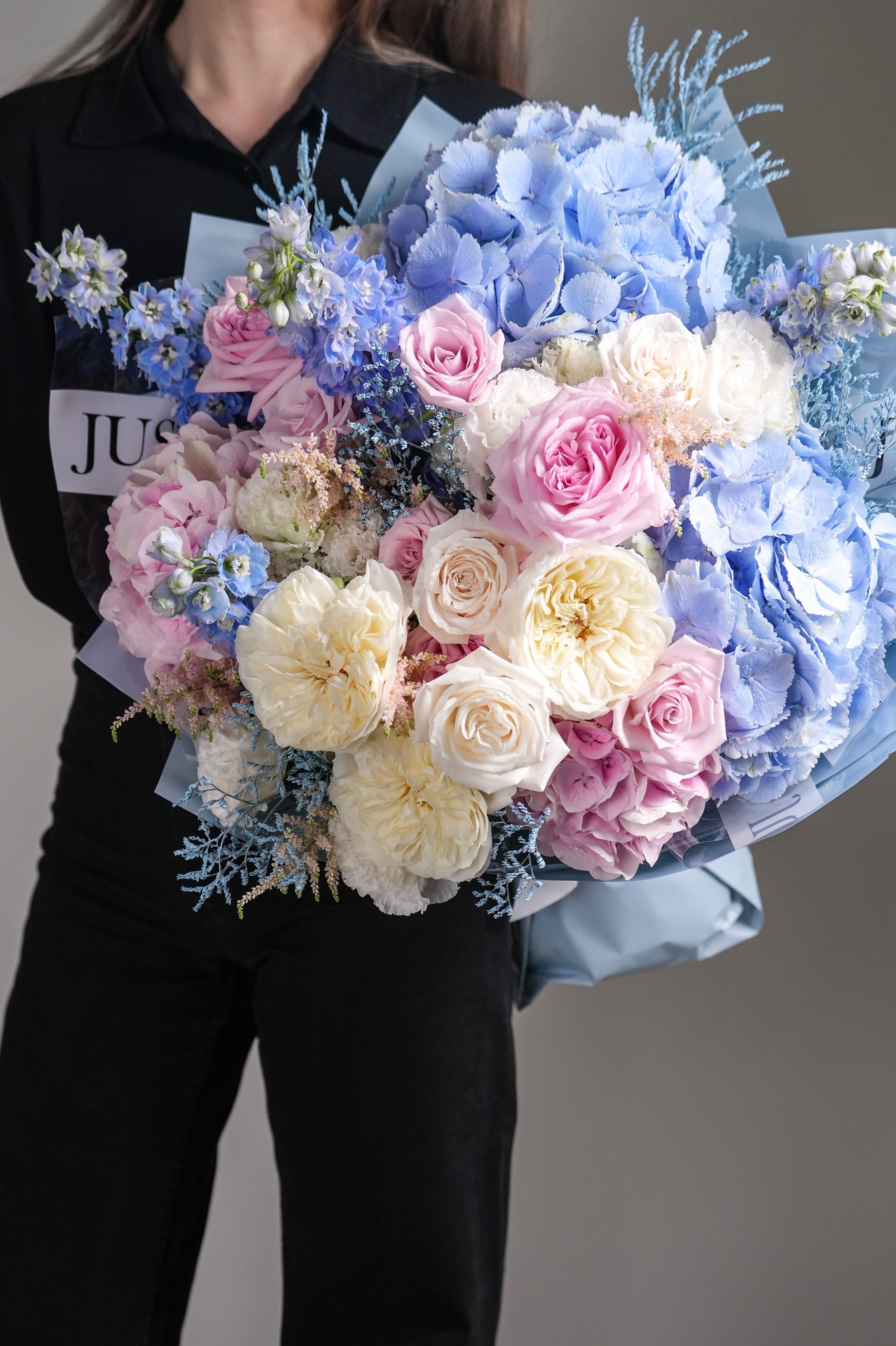 Mia bouquet with pastel blue hydrangeas, blush pink roses, white roses, and delphiniums