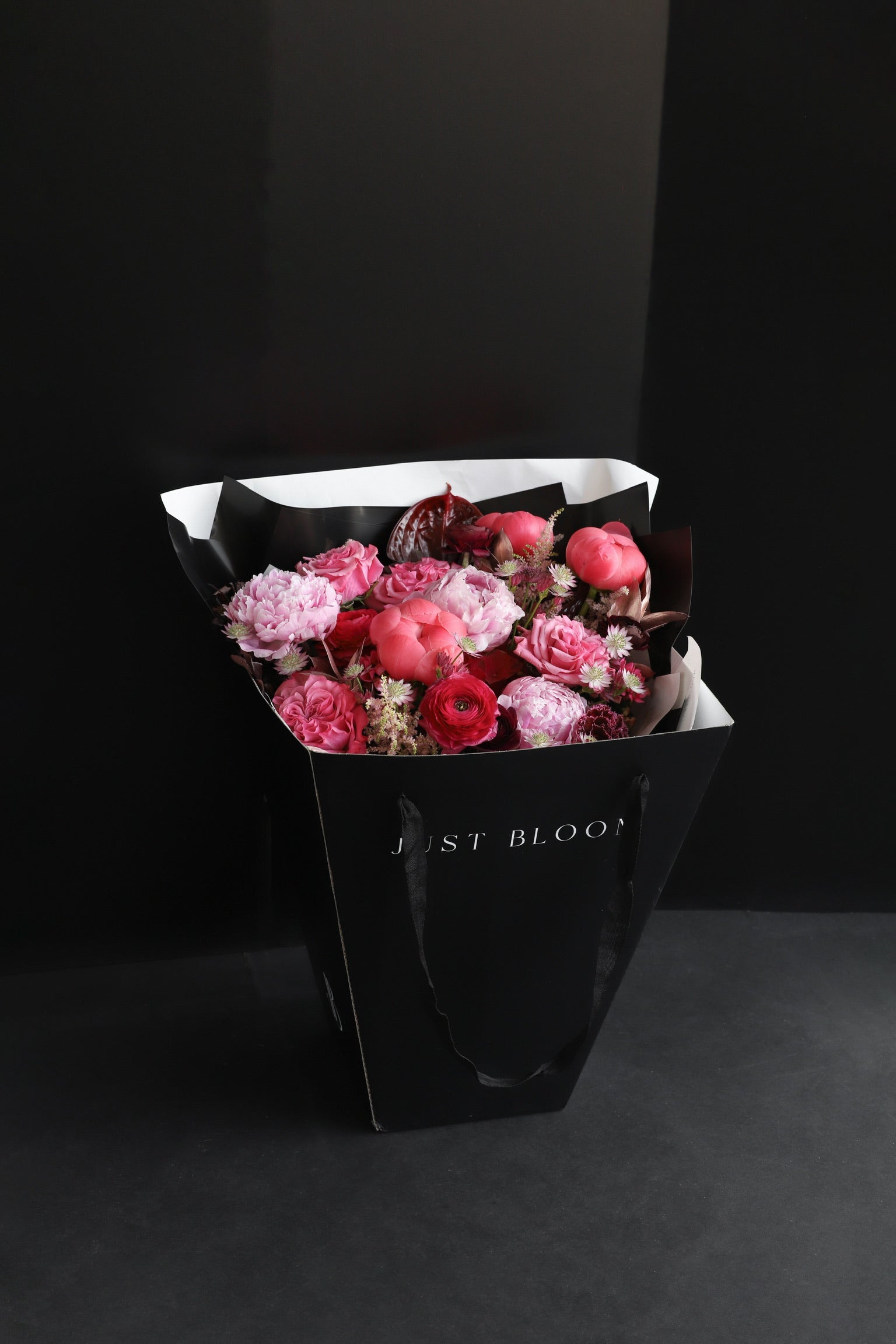 The Midnight Peonies luxury bouquet by Just Bloom Hong Kong presented in a black Just Bloom tote bag, showcasing abundant pink, coral and burgundy blooms