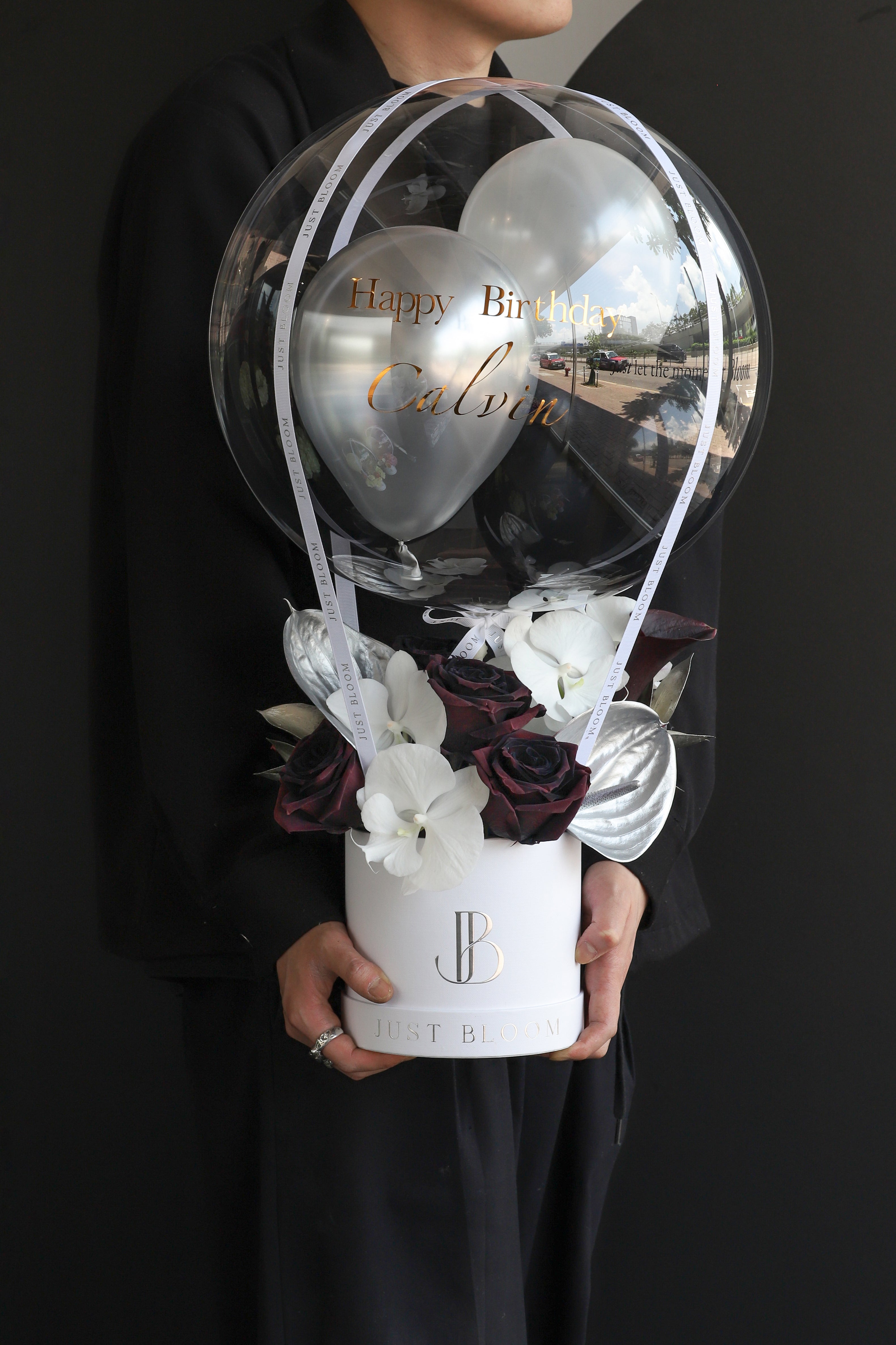 Model holding a dramatic flower box with deep burgundy roses, white orchids, and silver Anthuriums in a white Just Bloom round box against a dark background — Just Bloom Hong Kong