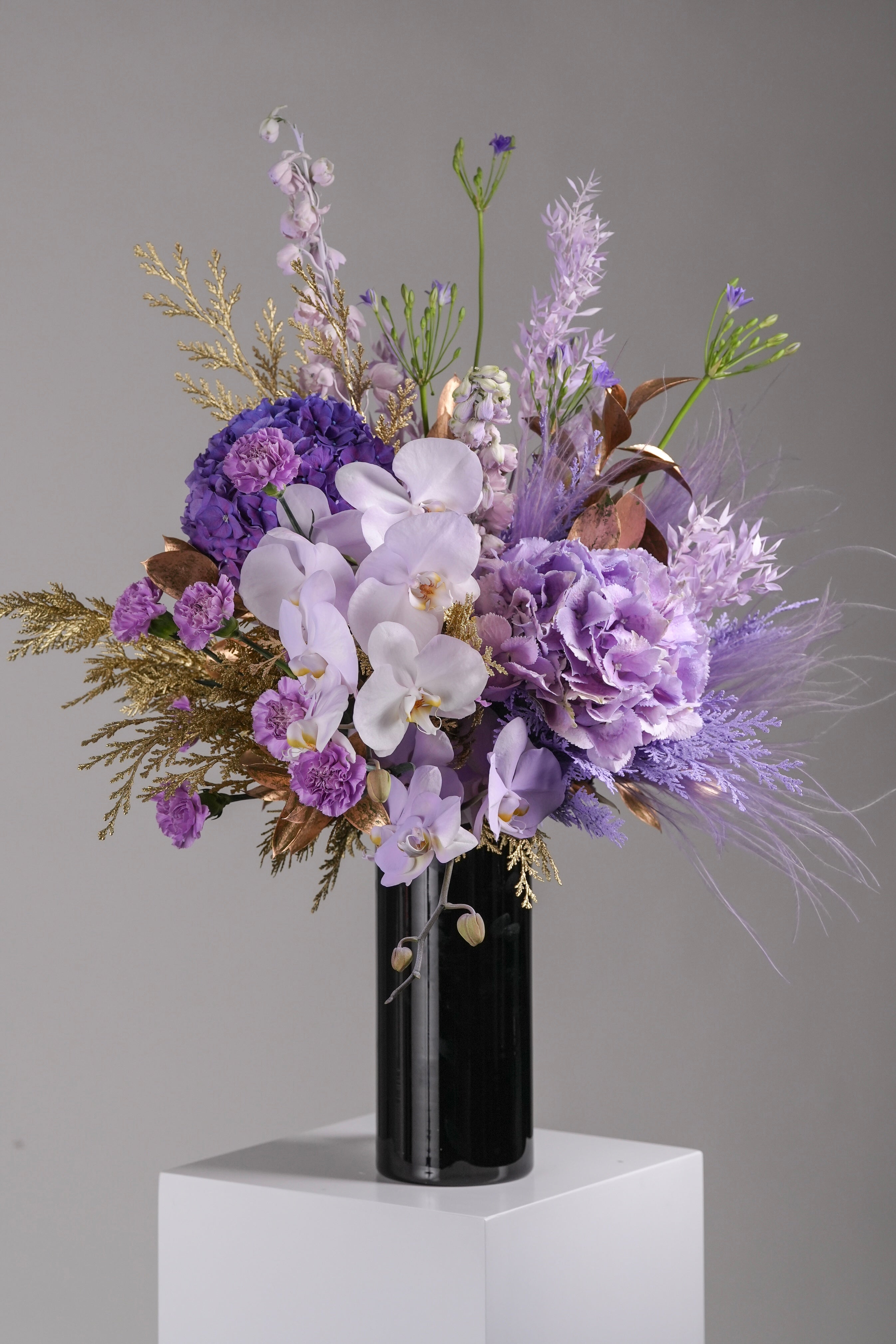 Morgana vase arrangement with purple hydrangeas, orchids, carnations, and gold leaves