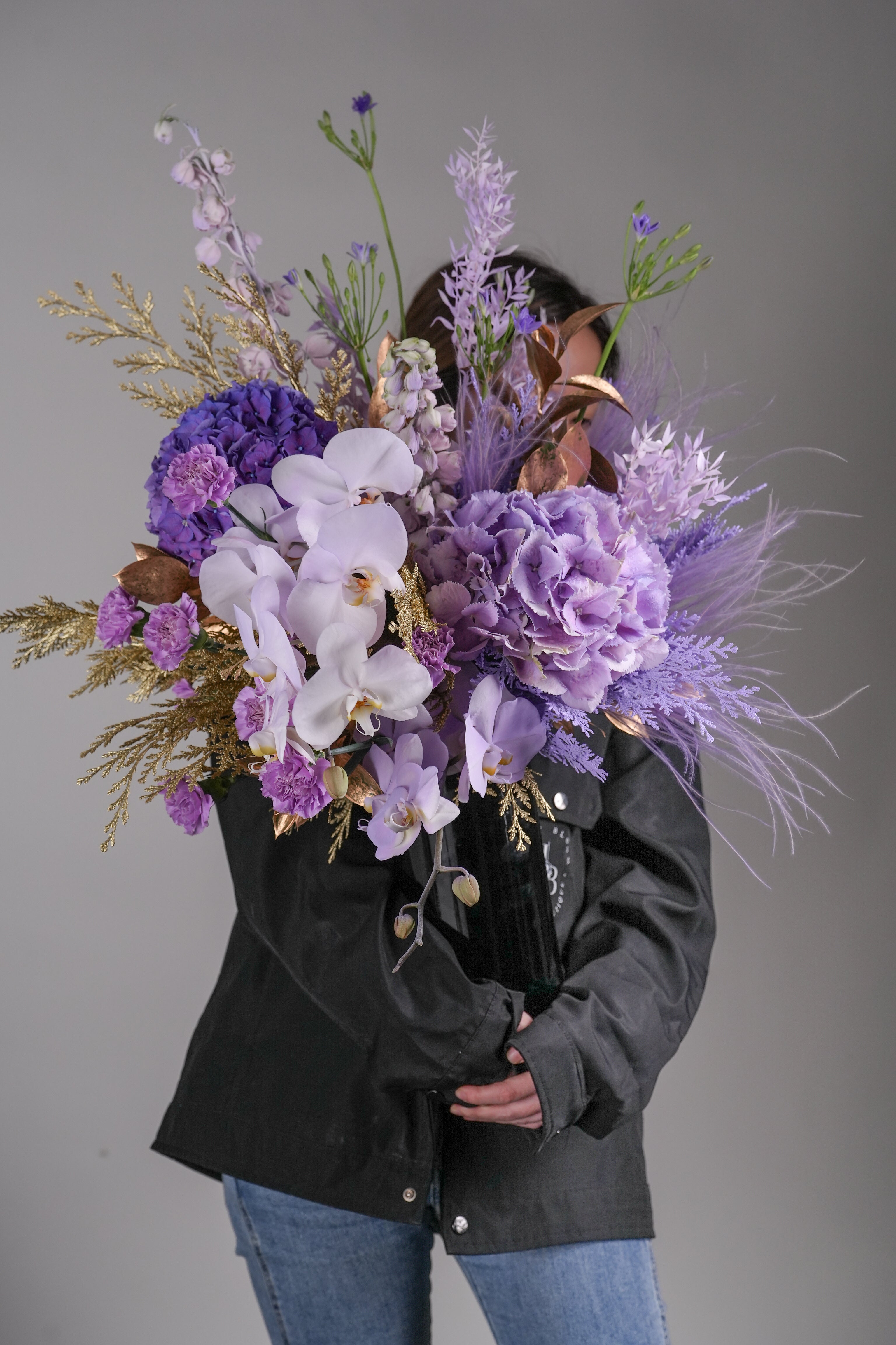 Morgana floral arrangement held in hand, featuring purple orchids and gold foliage