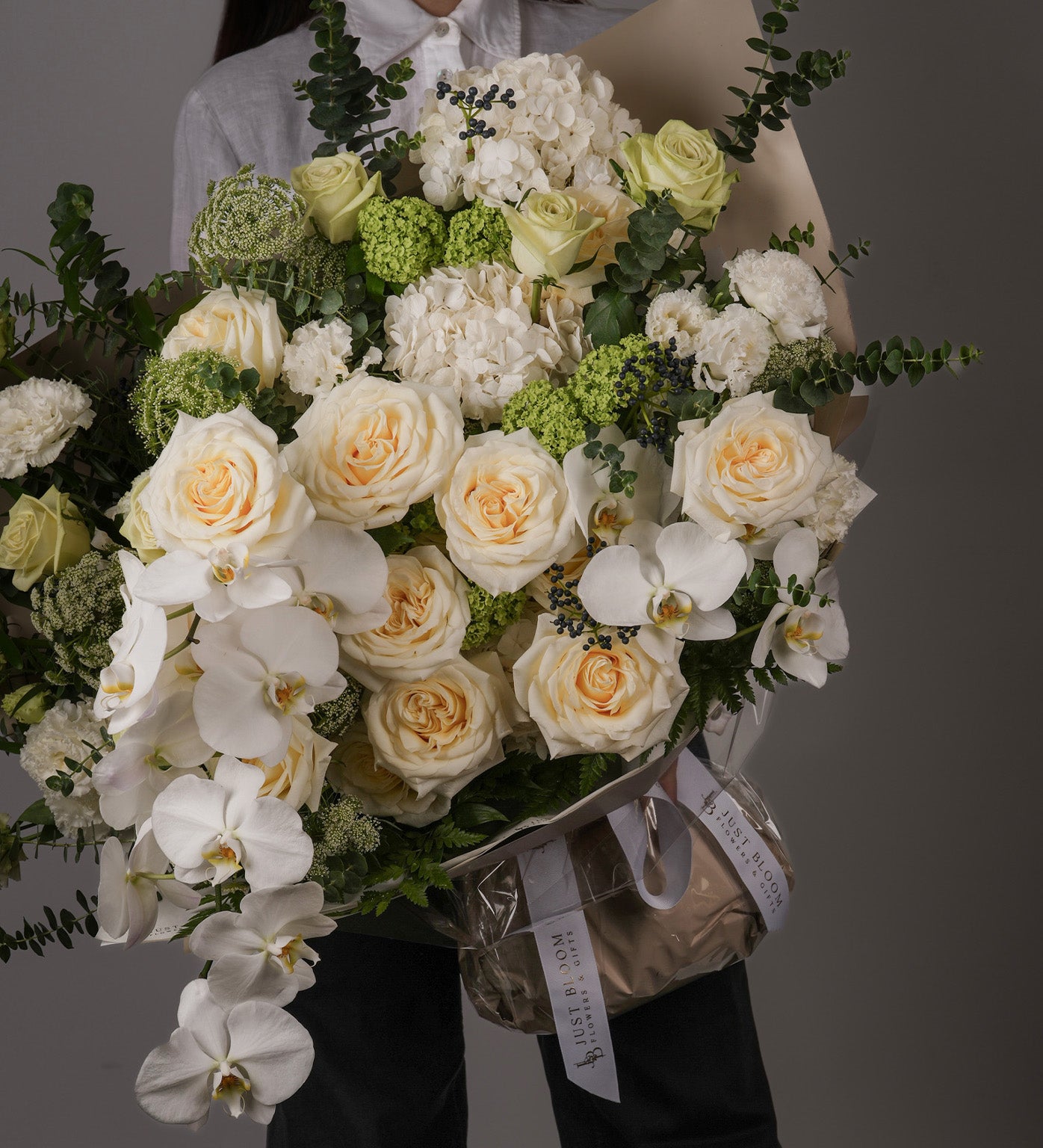 Nadia bouquet with cream Ecuadorian roses and white orchids, held from front view