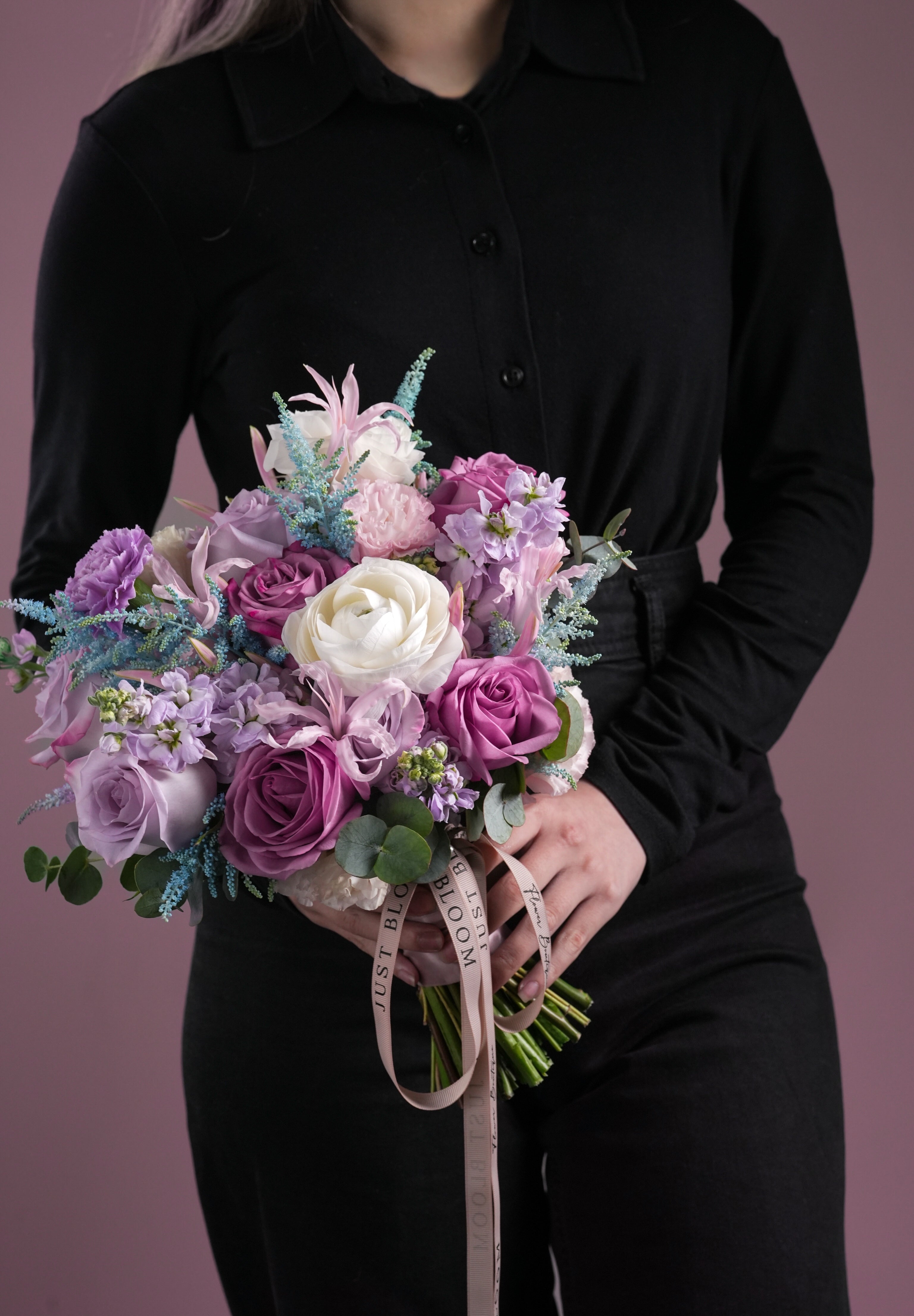 Naomi bridal bouquet held in both hands with purple roses, blue accents and soft pink florals