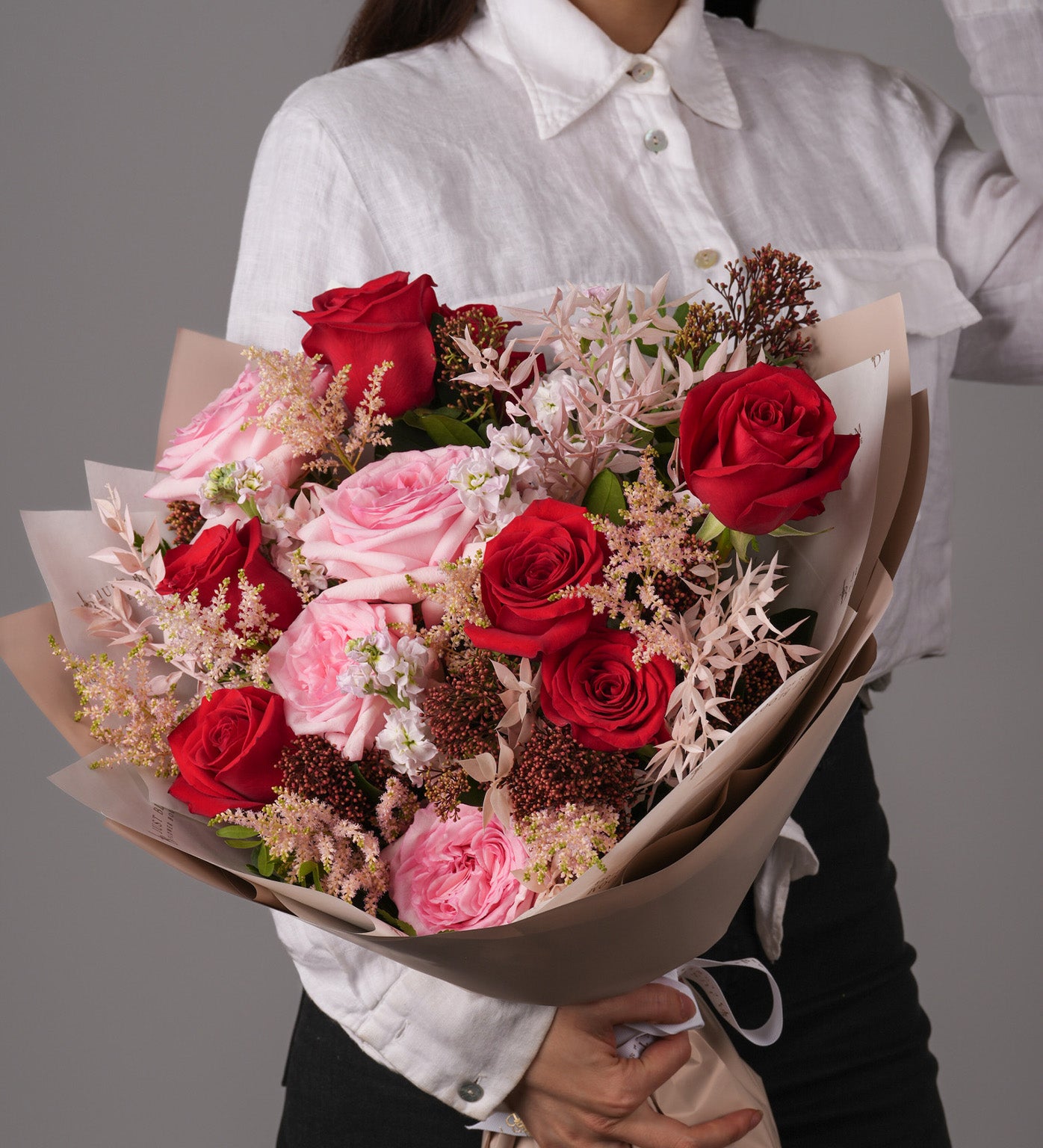 Noa bouquet handheld, featuring romantic red roses and soft pink blooms in layered wrapping