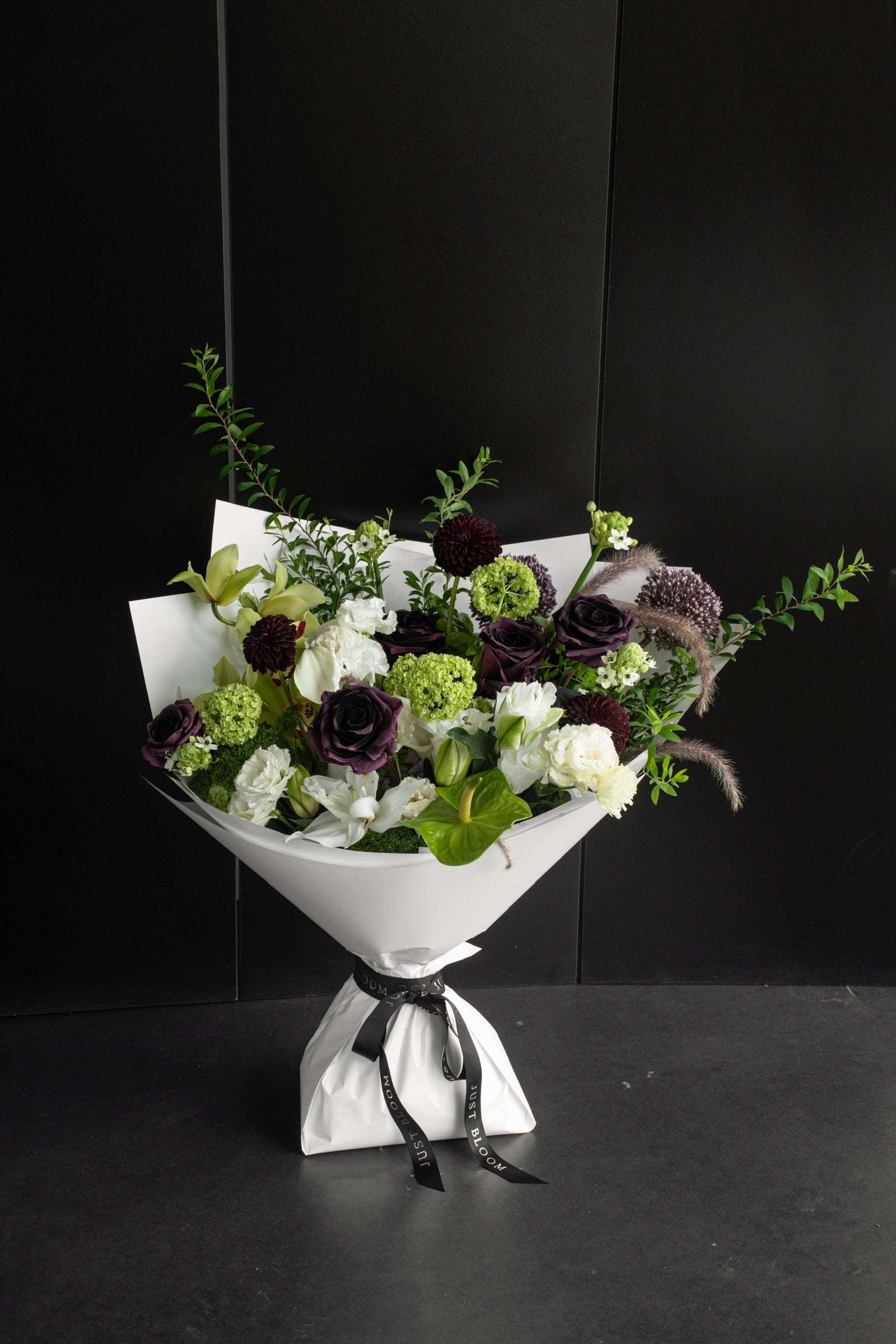 Large dark-toned fresh flower bouquet in deep plum, lime green, and white with mixed seasonal blooms and greenery wrapped in white Just Bloom paper against a dark background — Just Bloom Hong Kong