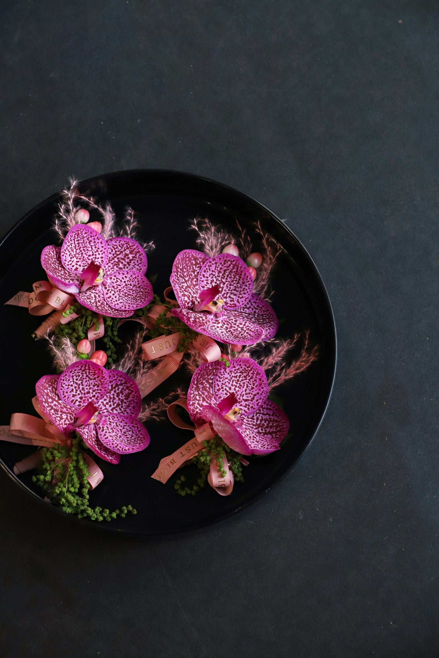 Close-up of four Orchid Edit wedding corsages on a black tray by Just Bloom Hong Kong, showcasing striking vanda orchids with intricate purple and pink patterning, pink broom bloom and Just Bloom rose gold ribbon