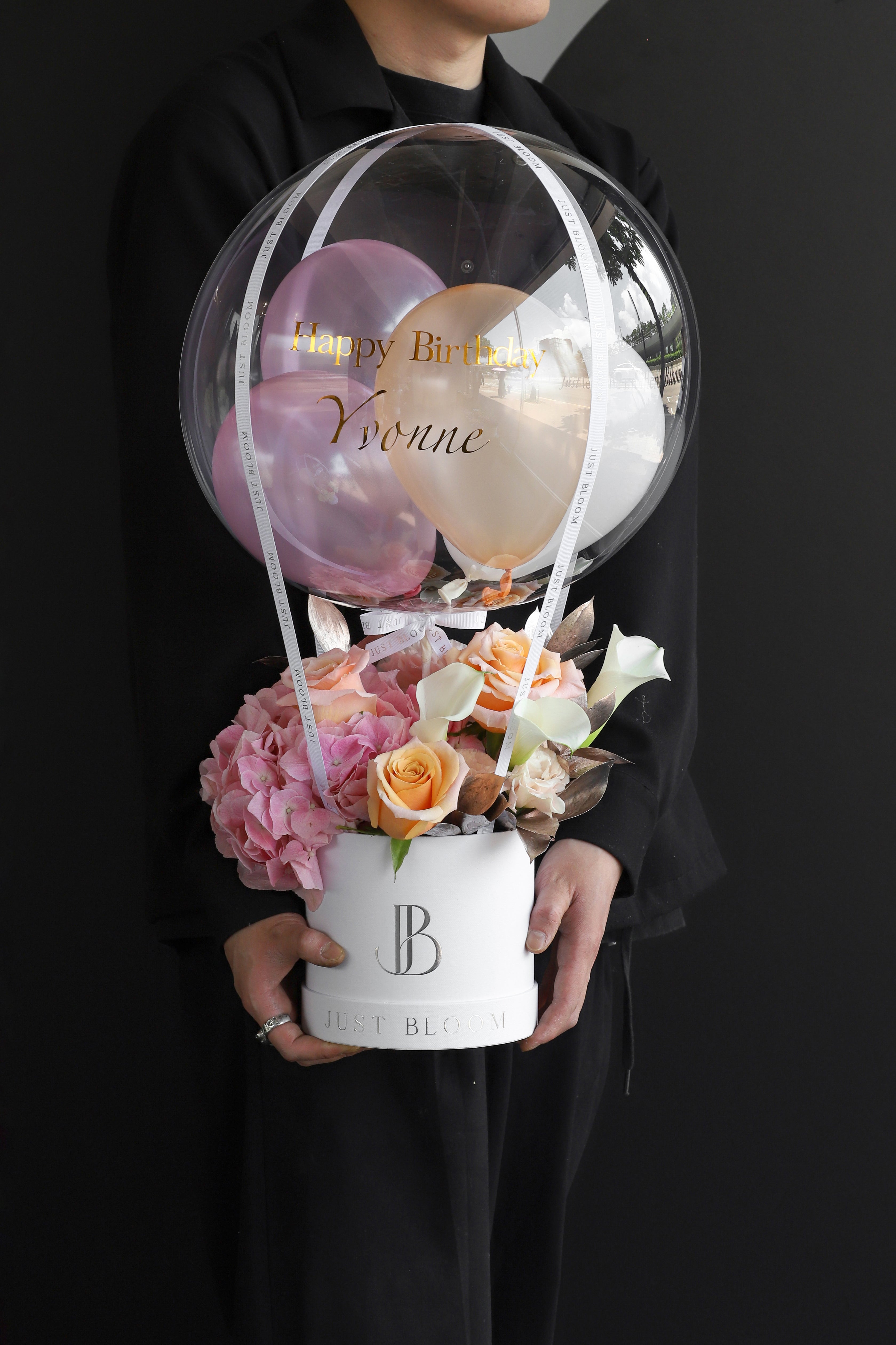 Model holding a fresh flower box with pink Hydrangeas, peach Roses, and white Calla Lilies in a white Just Bloom round box against a dark background — Just Bloom Hong Kong